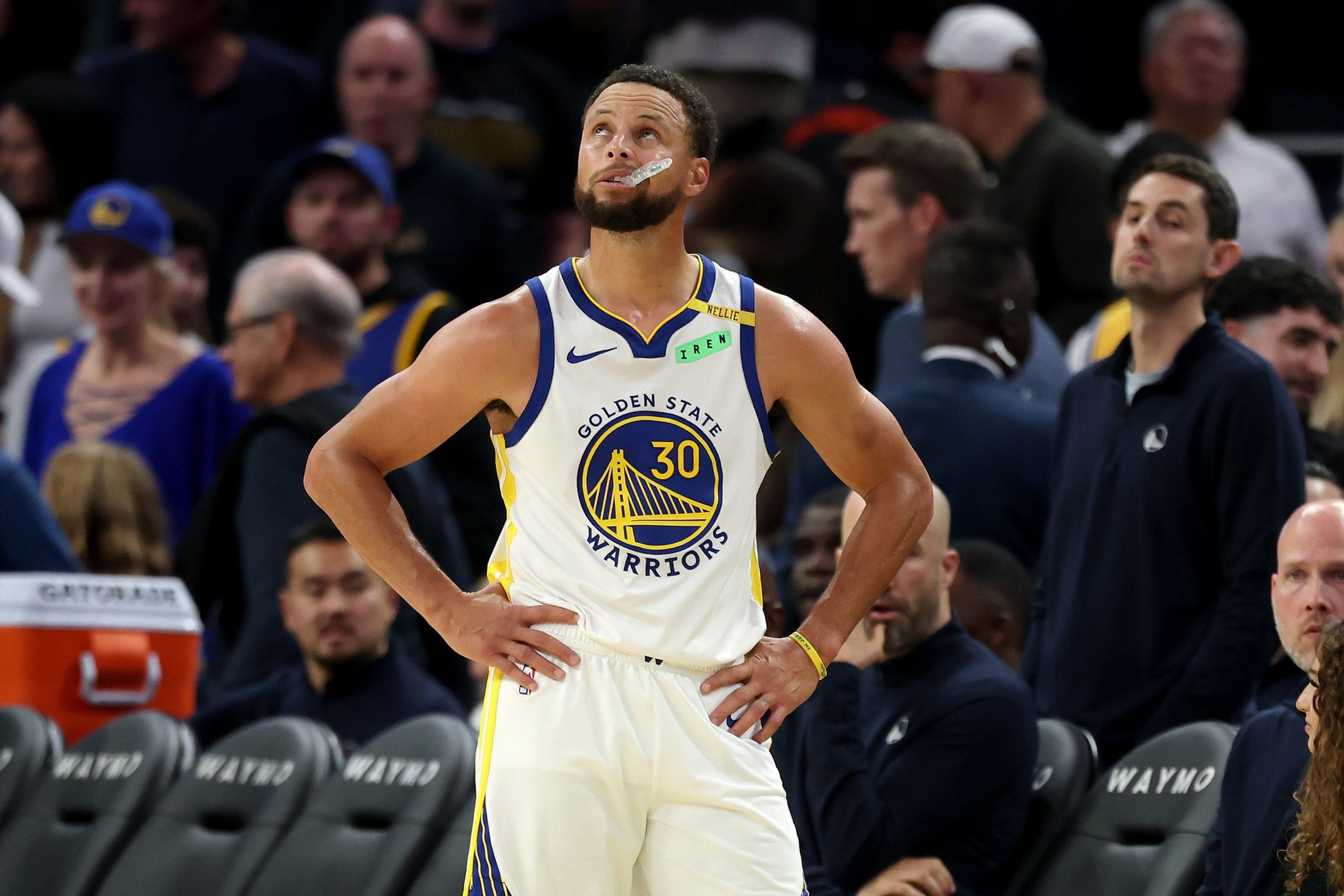 A basketball player in a Golden State Warriors jersey, number 30, stands with hands on hips looking upward, surrounded by spectators.