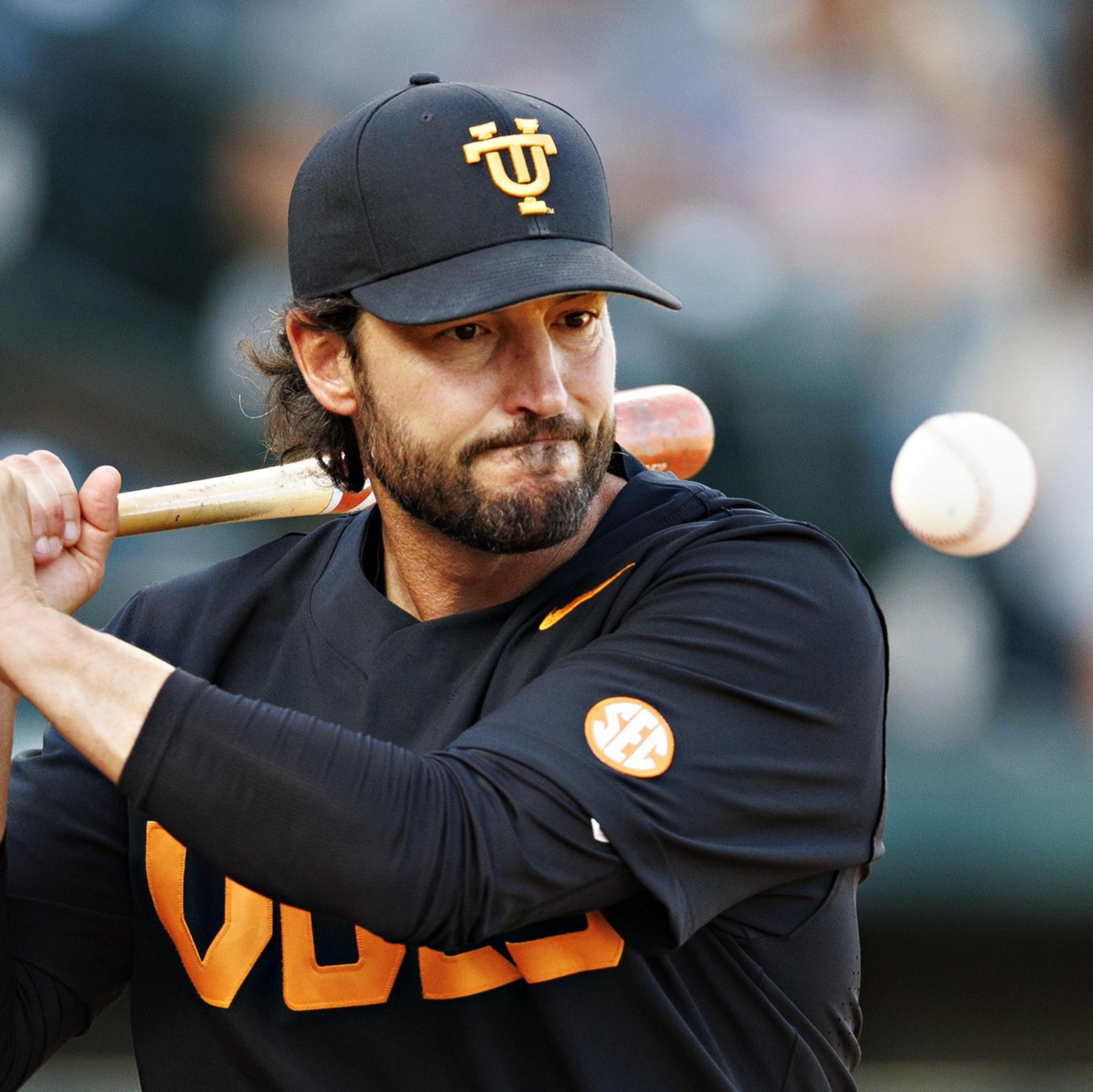 A baseball player wearing a black and orange uniform prepares to swing at an incoming ball with intense focus.
