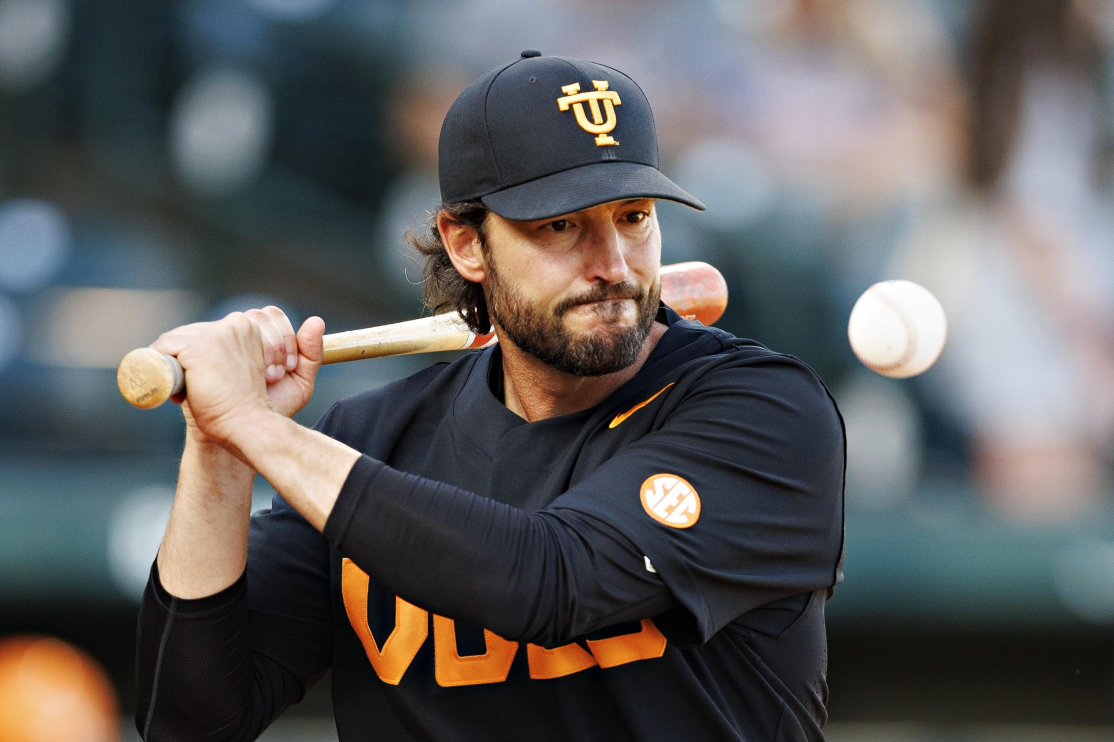 A baseball player wearing a black and orange uniform prepares to swing at an incoming ball with intense focus.