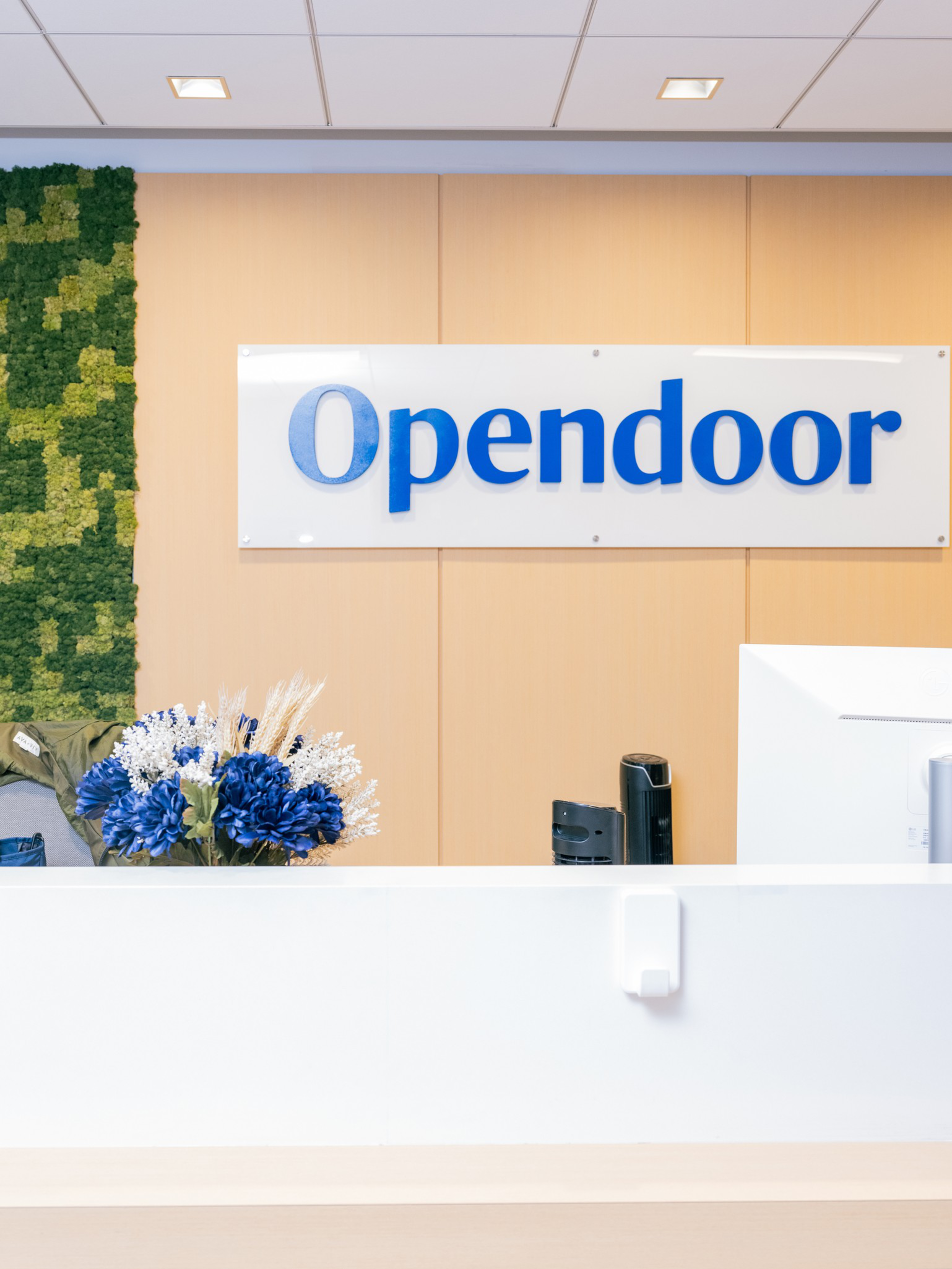 A reception desk with a bright bouquet of blue and white flowers, a computer, and a sign on the wall behind that reads “Opendoor.”