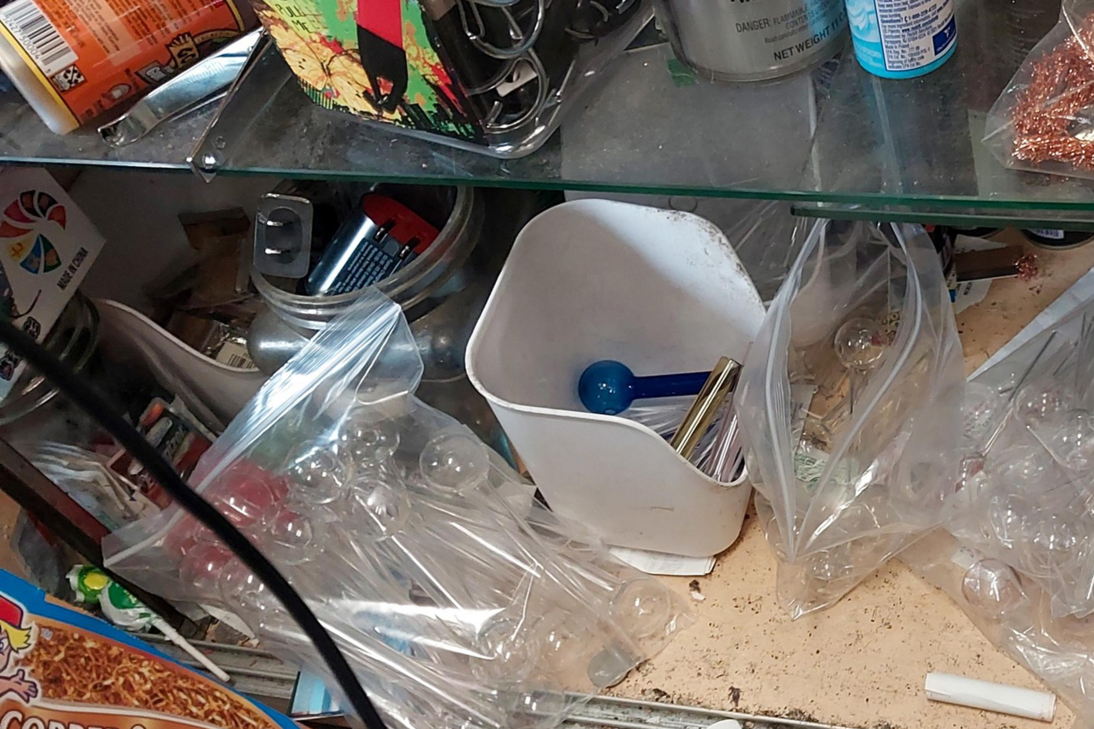 The image shows a cluttered shelf with various items, including batteries, copper scrubbers, plastic bags, and a container with a blue scoop.