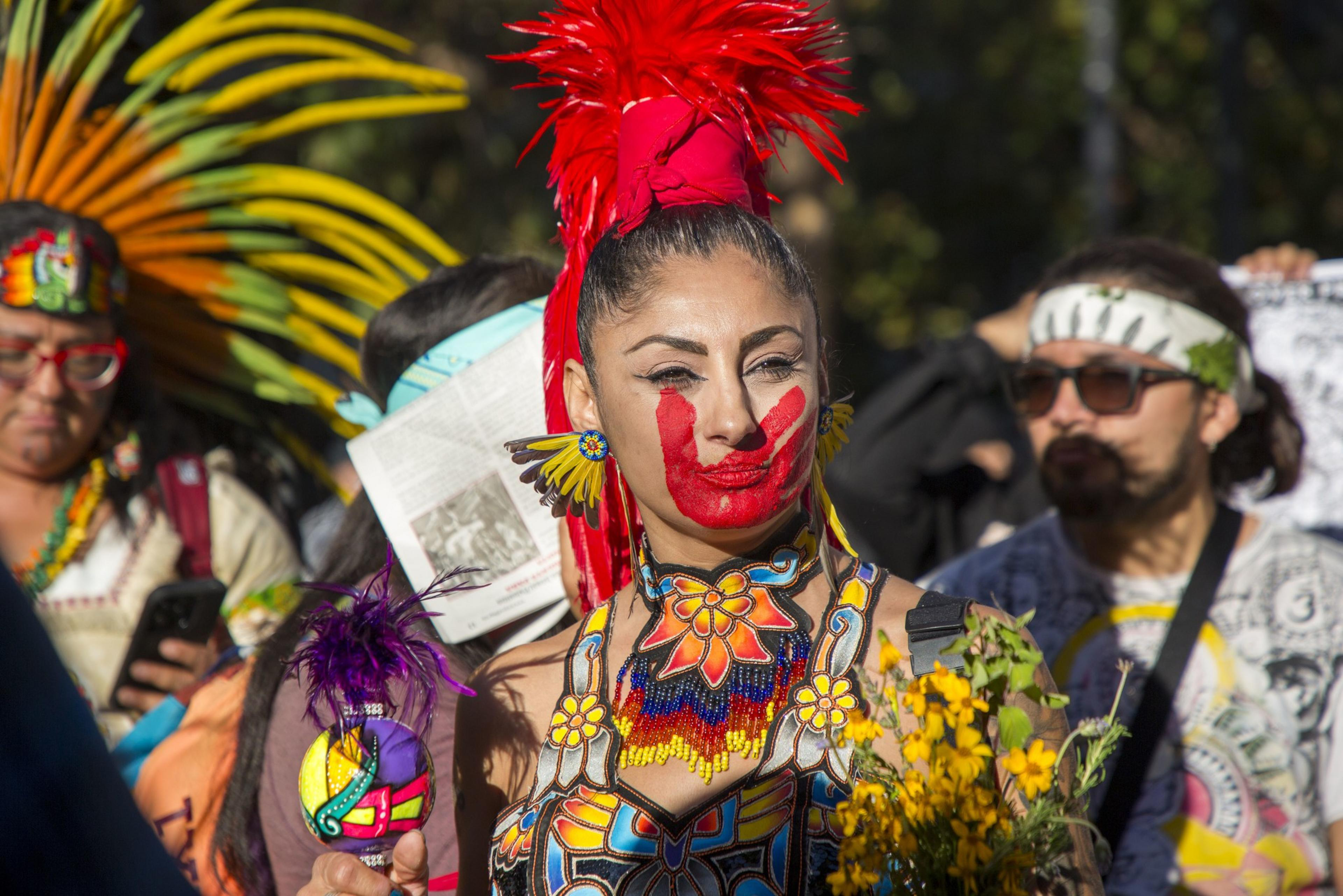 A protester wearing traditional clothing with a red hand-painted mark on their face.
