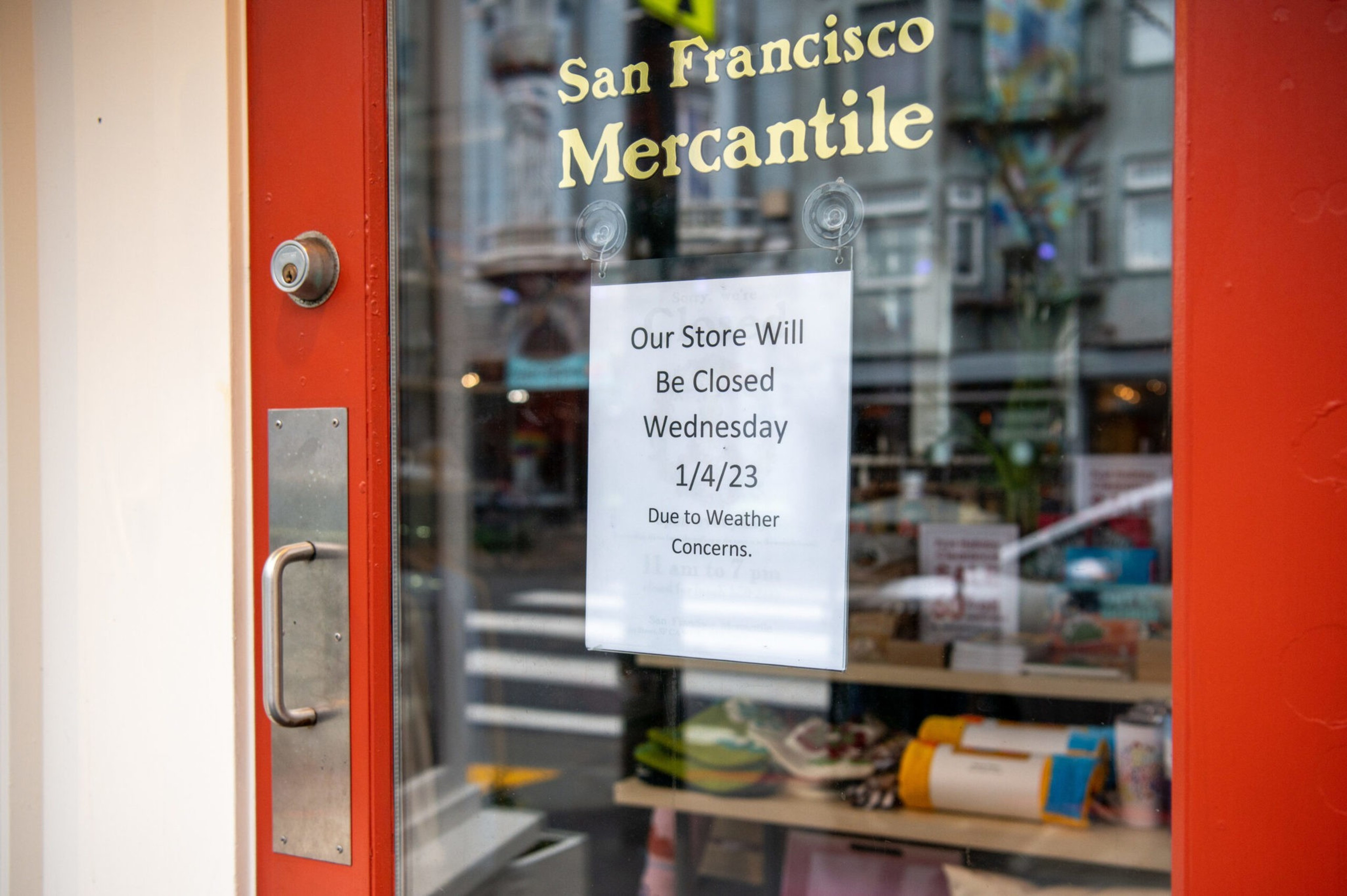 A glass door with a red frame shows a sign stating the San Francisco Mercantile store will be closed on 1/4/23 due to weather concerns.