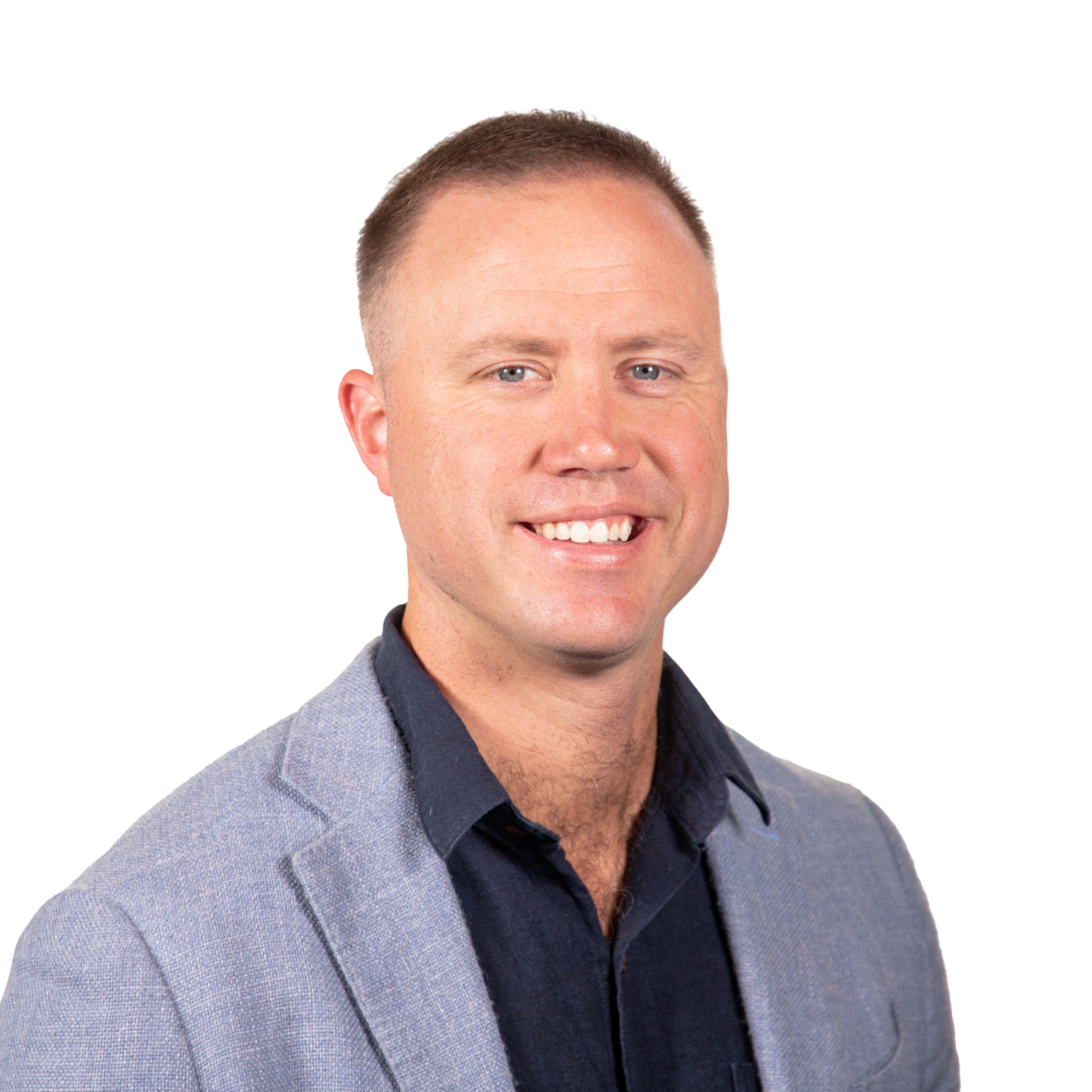 A man with short light brown hair smiles, wearing a light gray blazer over a dark navy shirt, against a plain white background.