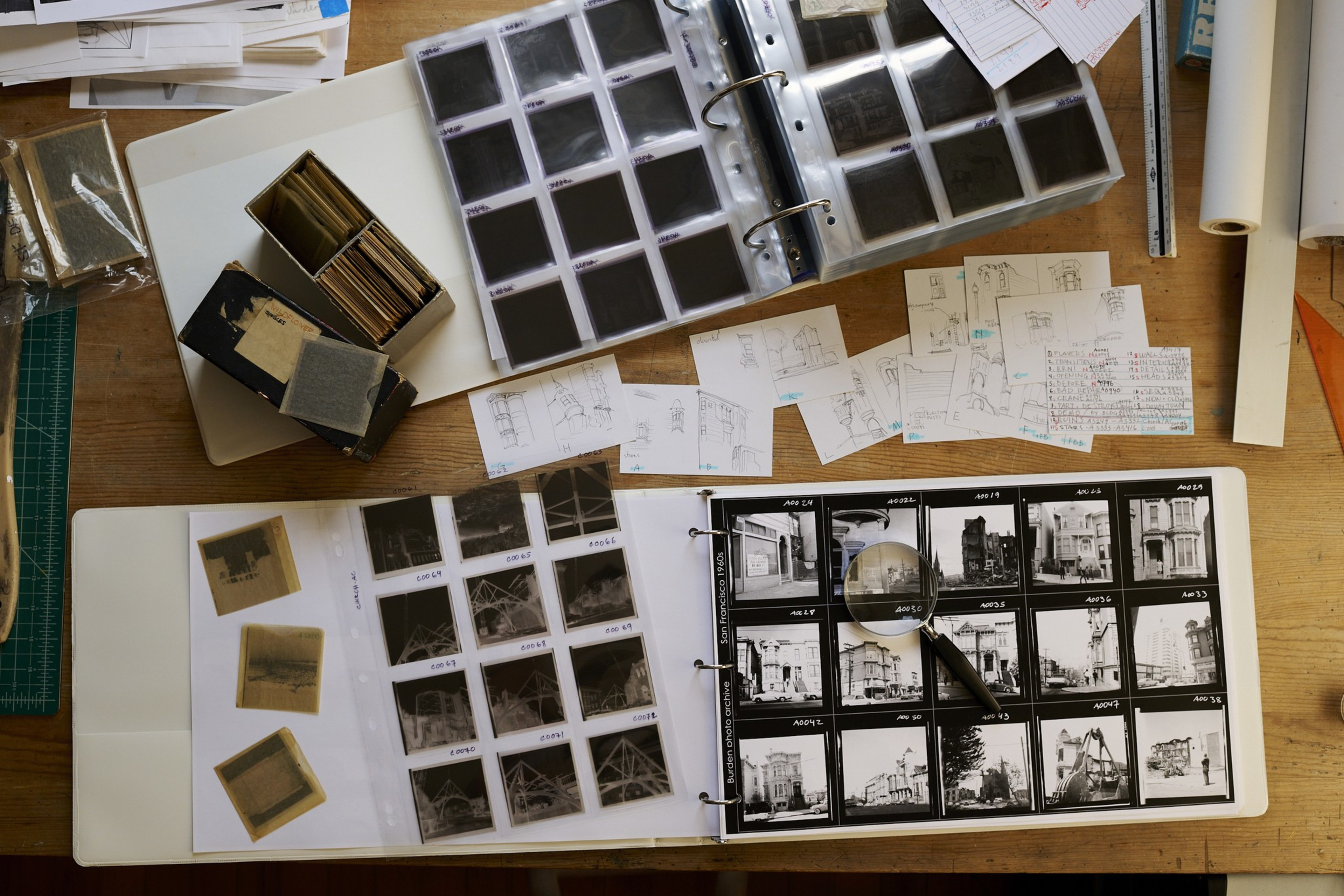 A desk with photo albums, negatives, sketches, and a magnifying glass.