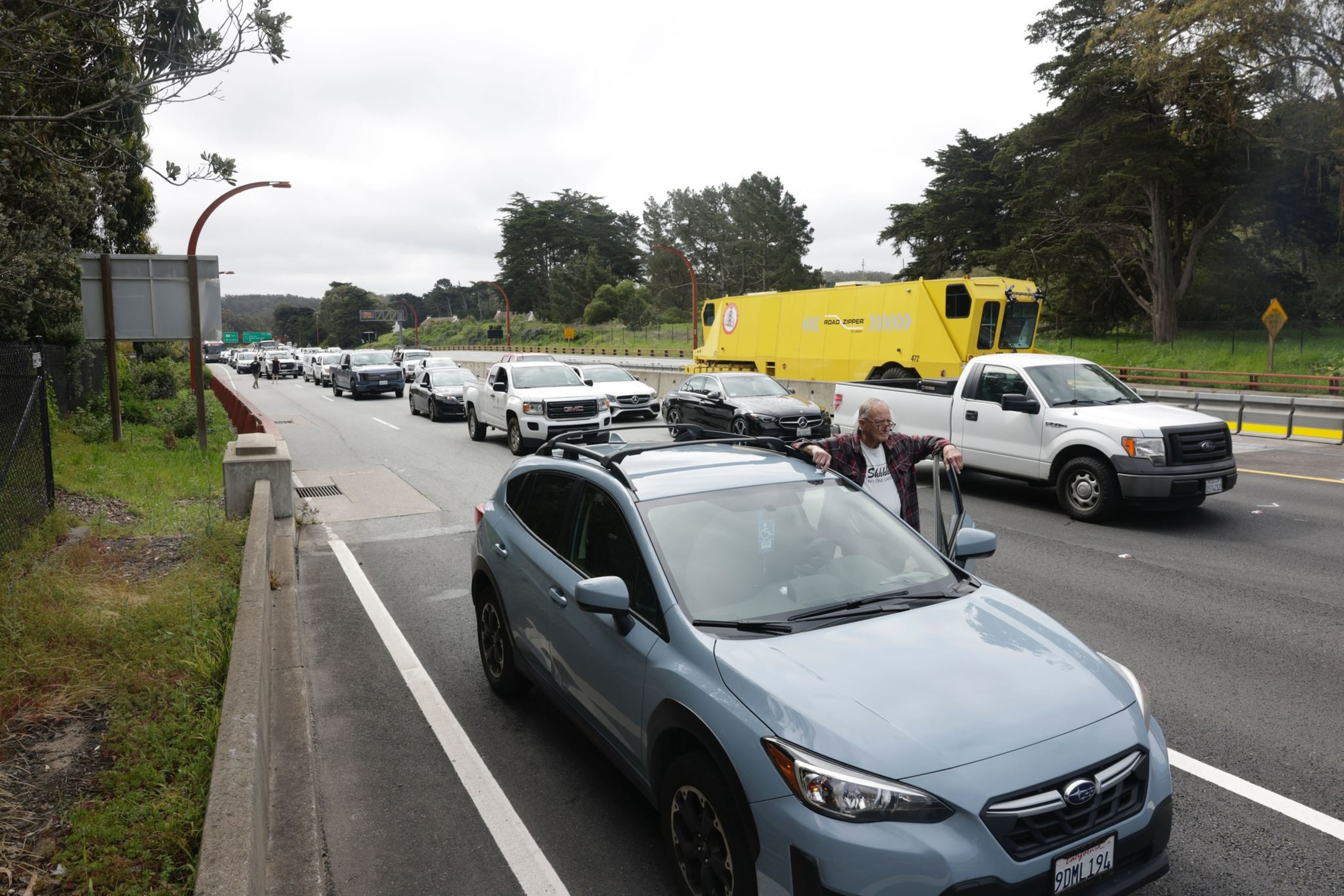 Traffic jam on a road with a man standing beside his car, looking frustrated.