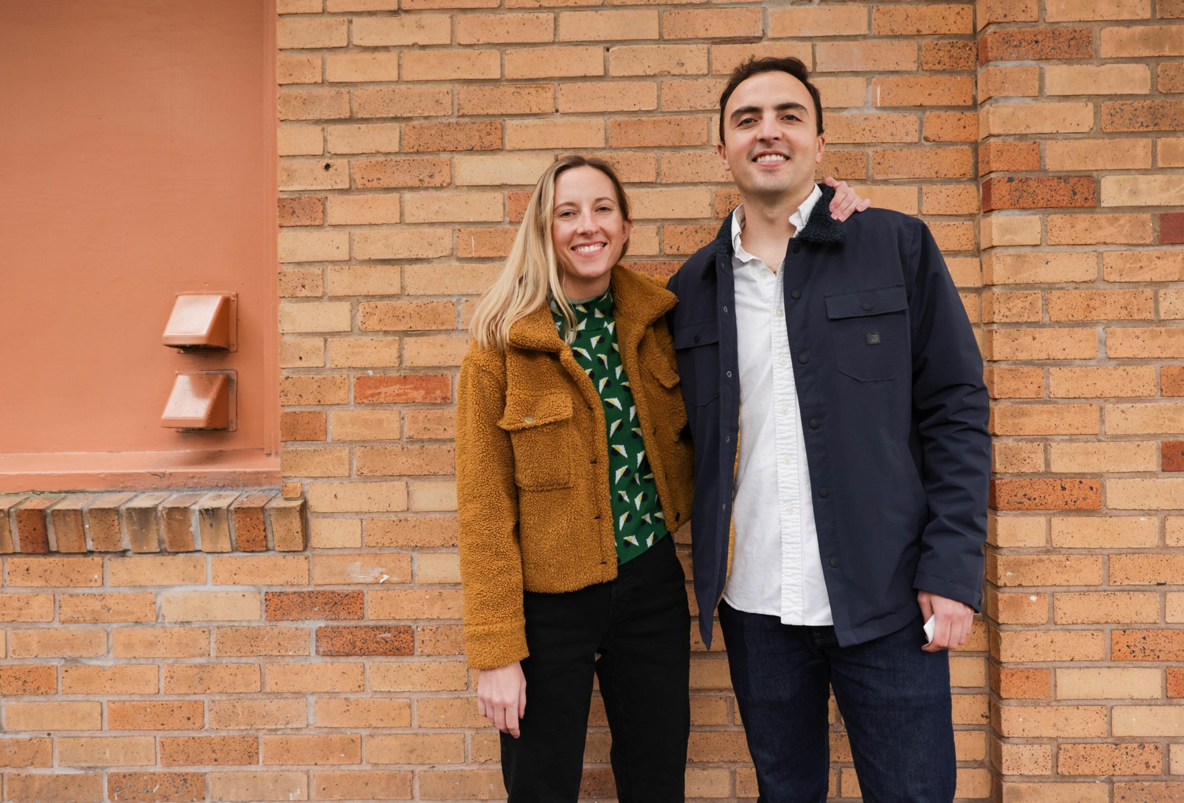 woman and man embrace by brick wall