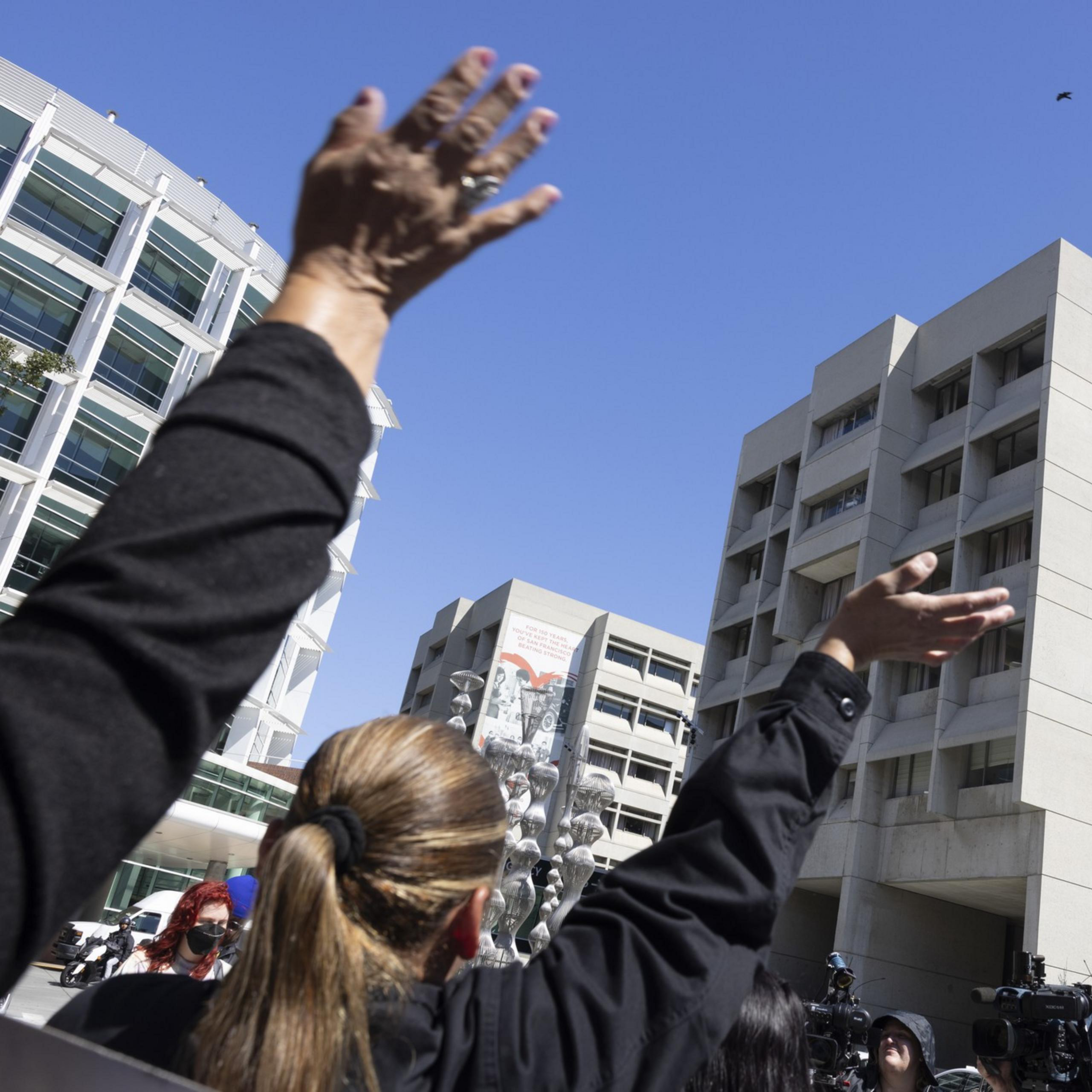 People are raising their hands in front of modern buildings under a ...