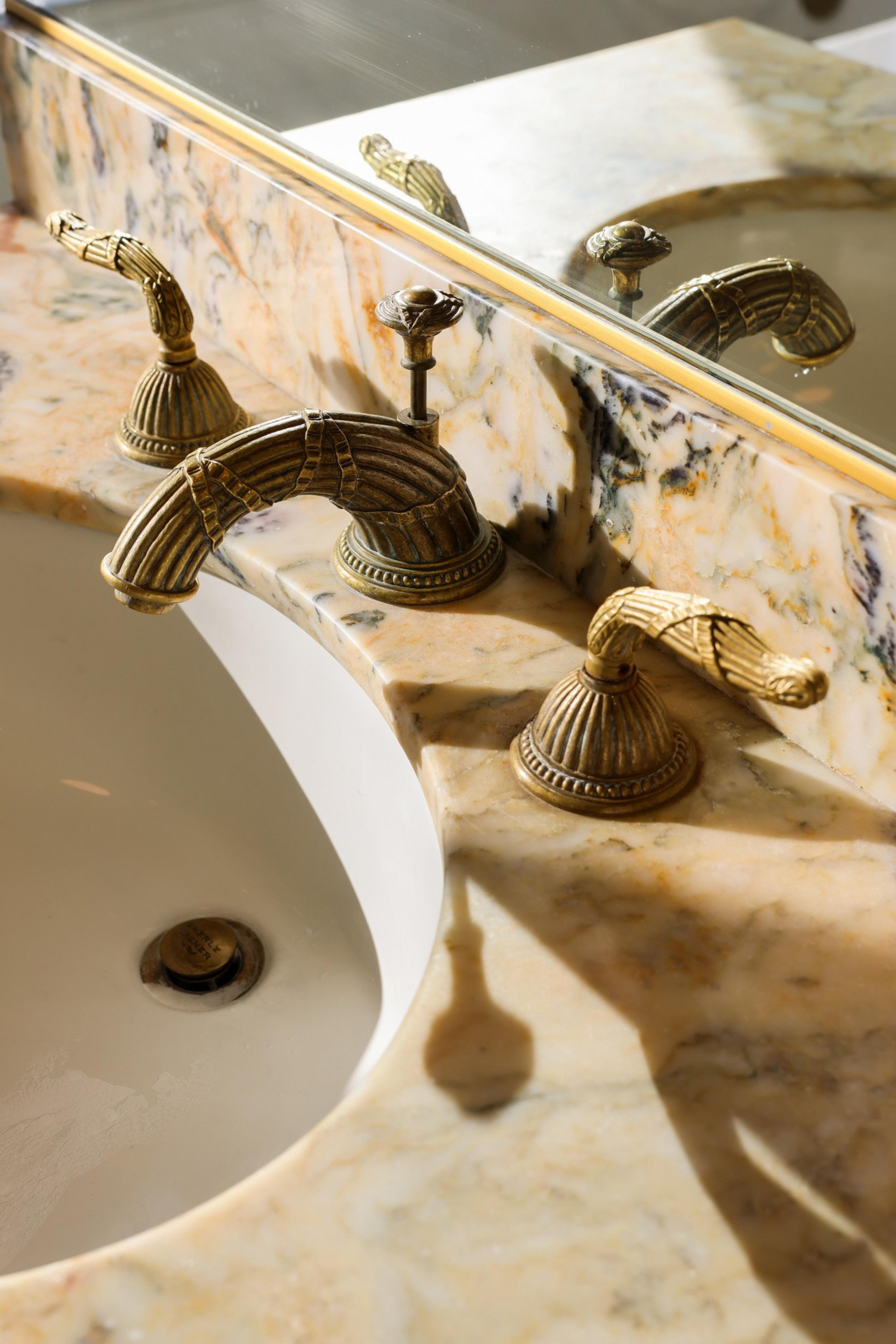 A marble sink countertop features ornate brass fixtures with intricate detailing and a mirror reflecting the faucet design.
