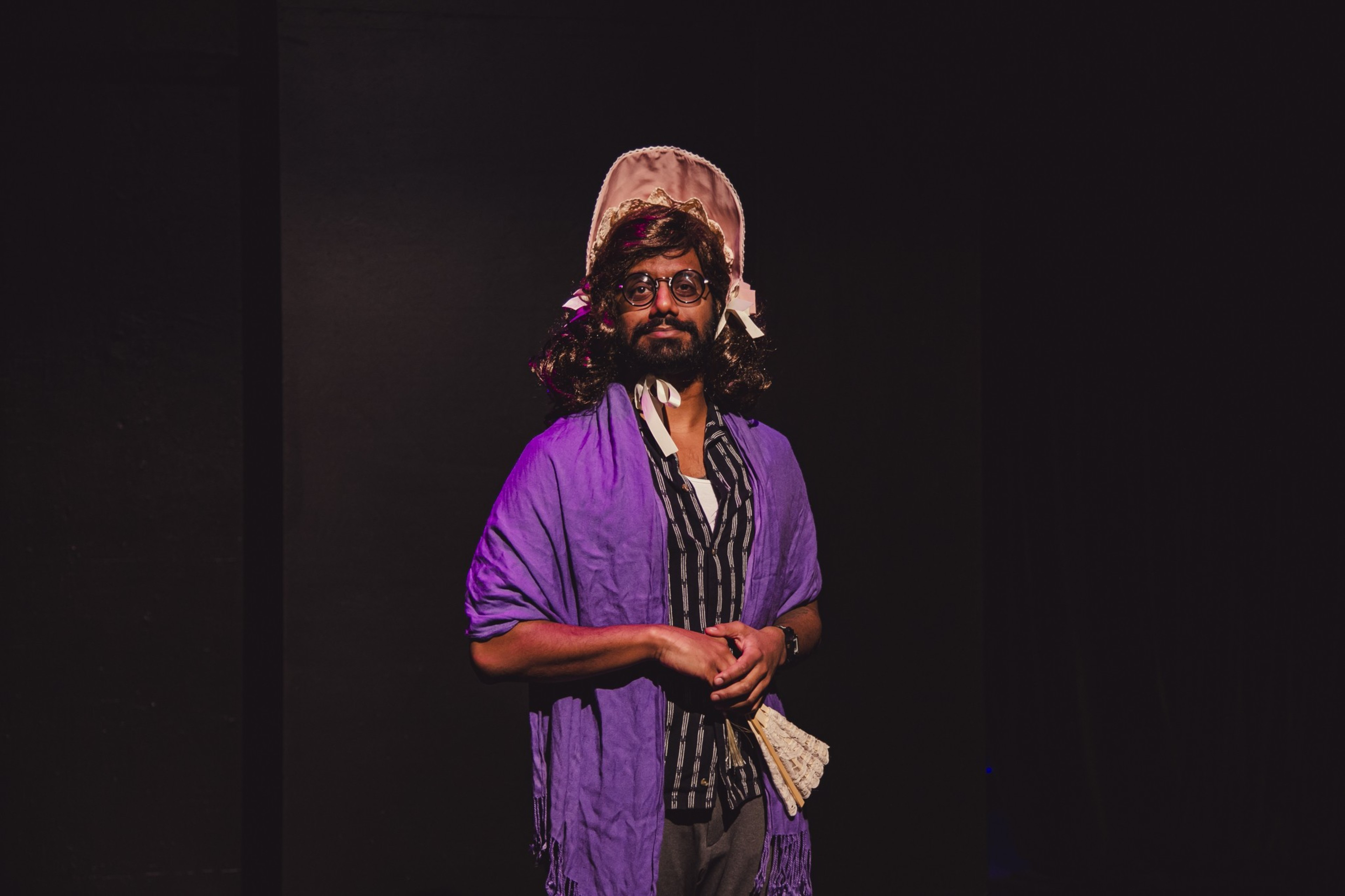 A man stands against a black backdrop wearing a bonnet.