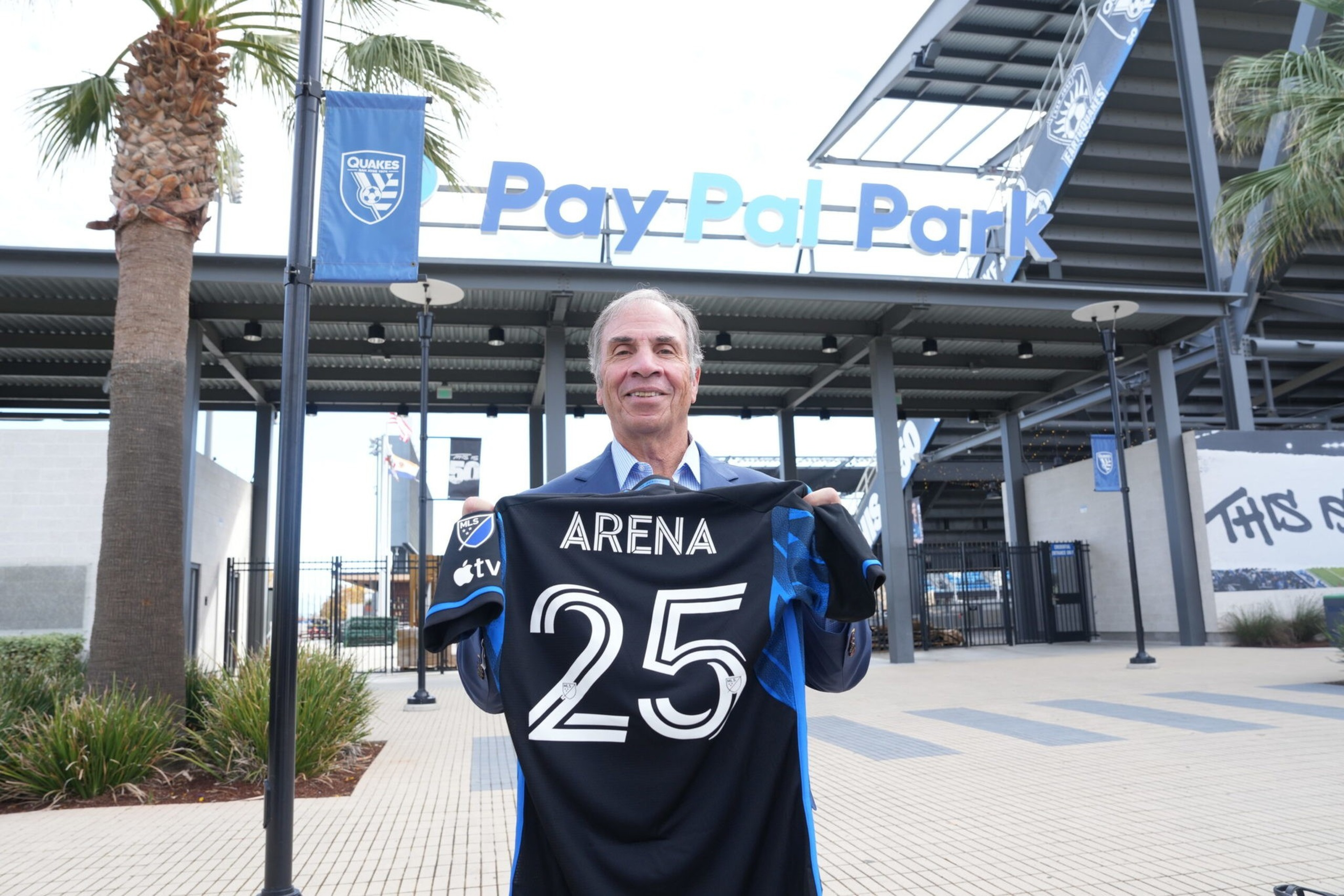 A man stands outside PayPal Park holding a black and blue soccer jersey with the name “ARENA” and number “25" on it.