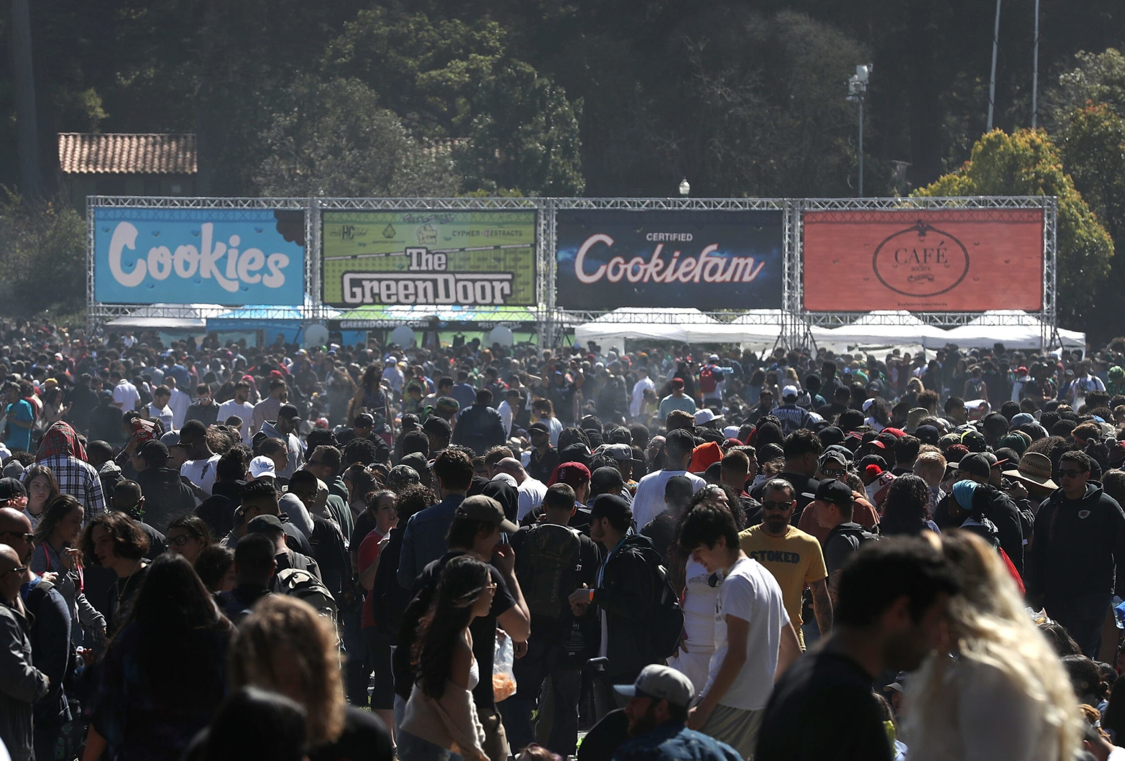 A crowded outdoor event with large banners reading &quot;Cookies&quot; and &quot;The Green Door.&quot;