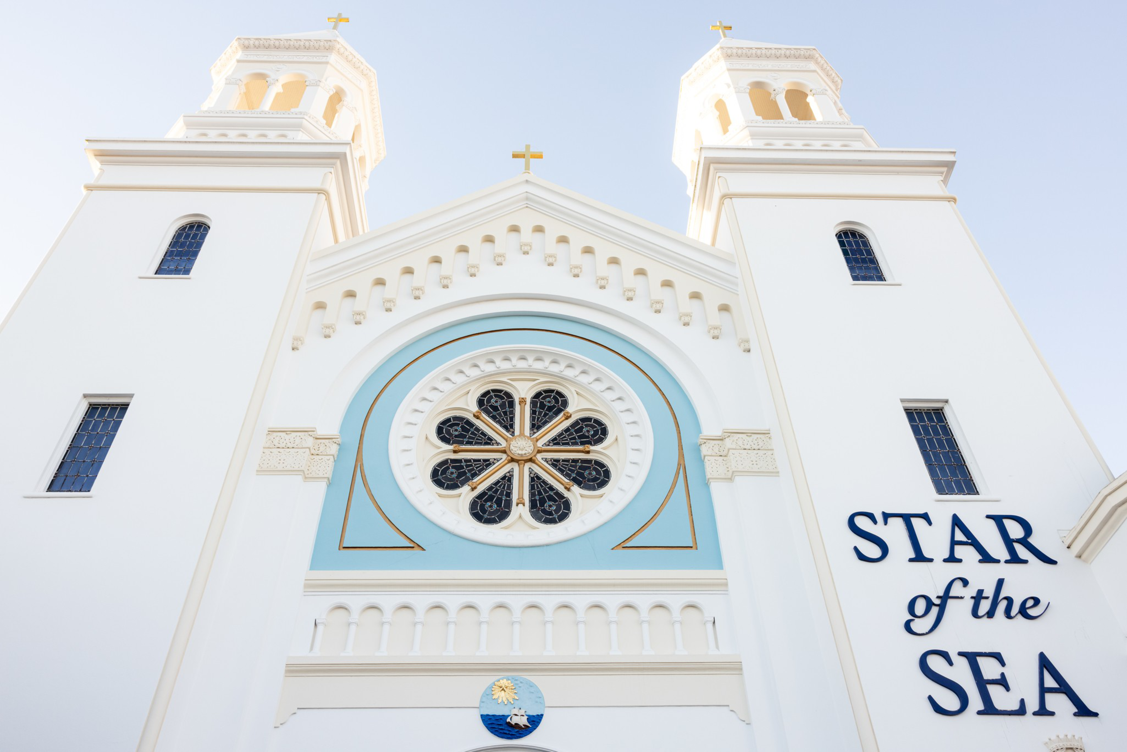 A white church facade with two towers, a circular stained glass window, gold crosses, and the words “STAR of the SEA” in blue letters.