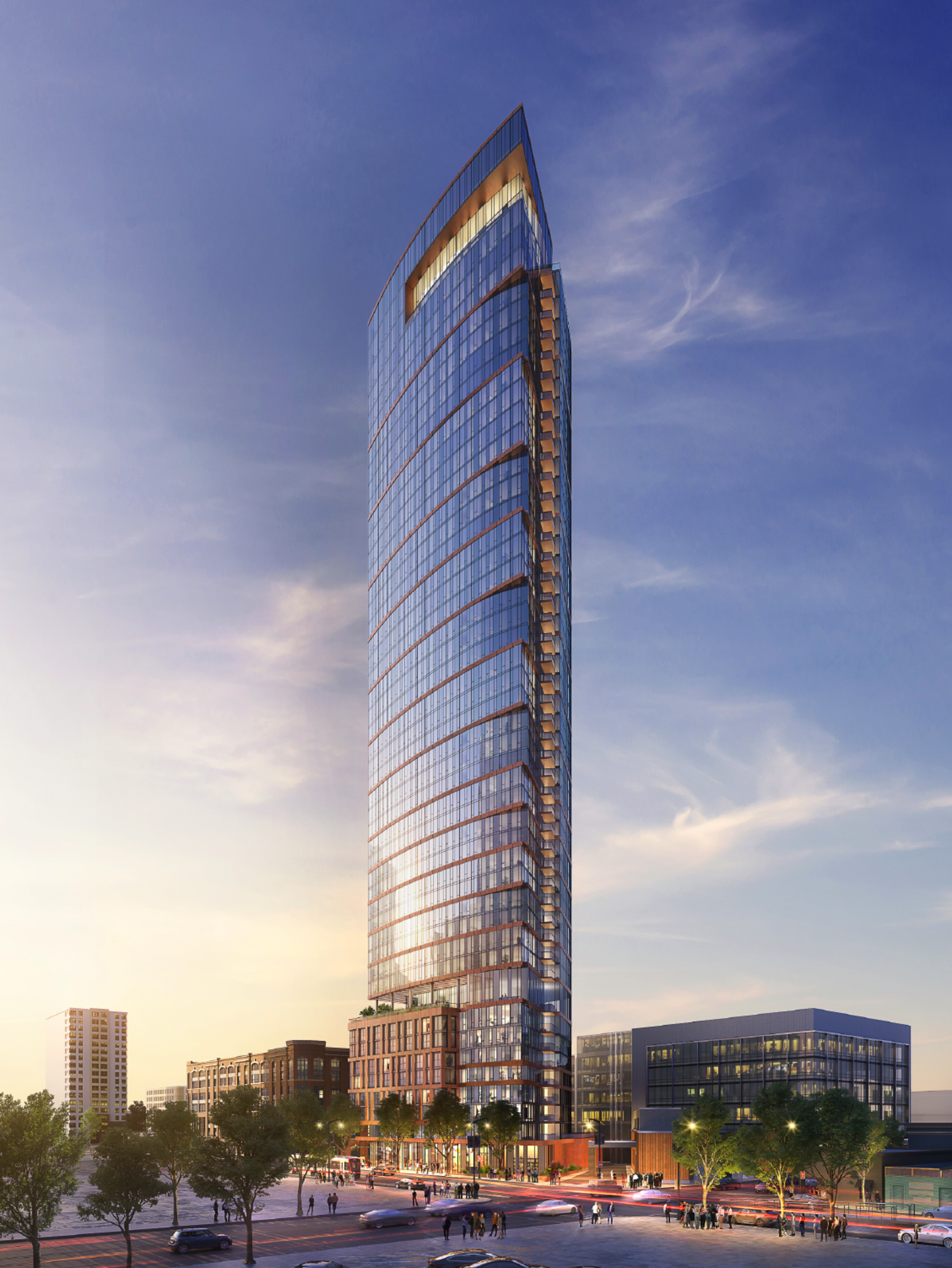 A tall, modern glass skyscraper with a curved top rises above smaller buildings, surrounded by trees and bustling streets under a partly cloudy sky at sunset.
