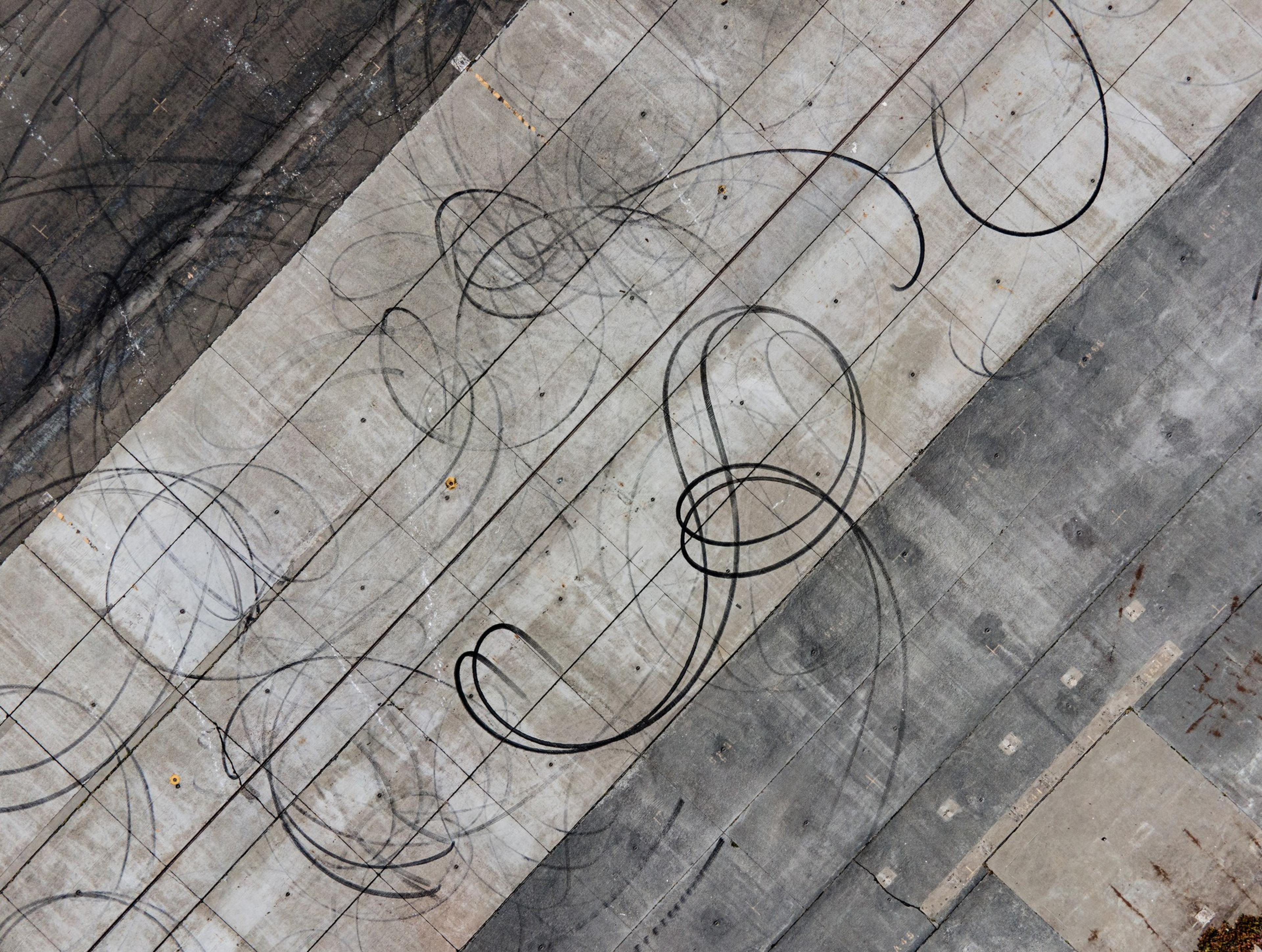 The image shows an aerial view of a concrete surface with looping tire skid marks on it, suggesting vehicle activity like drifting or spinning.from above. 
