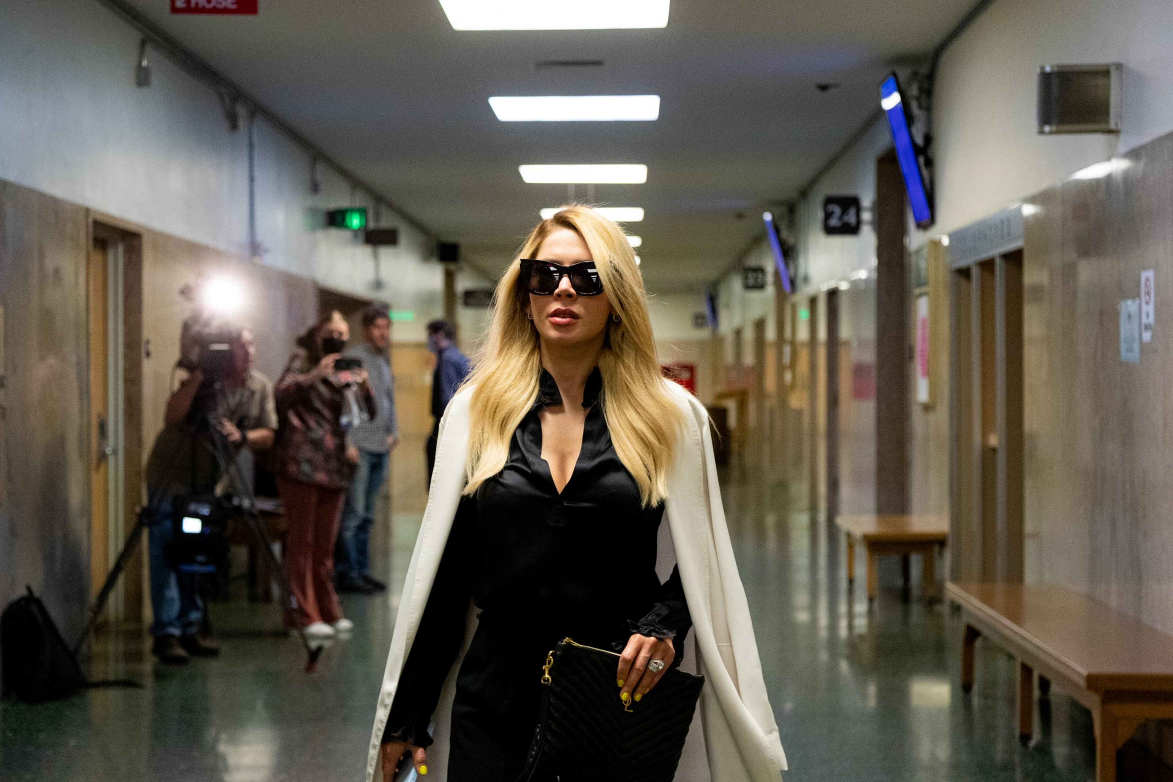 a woman in a white cape and sunglasses walks down a corridor