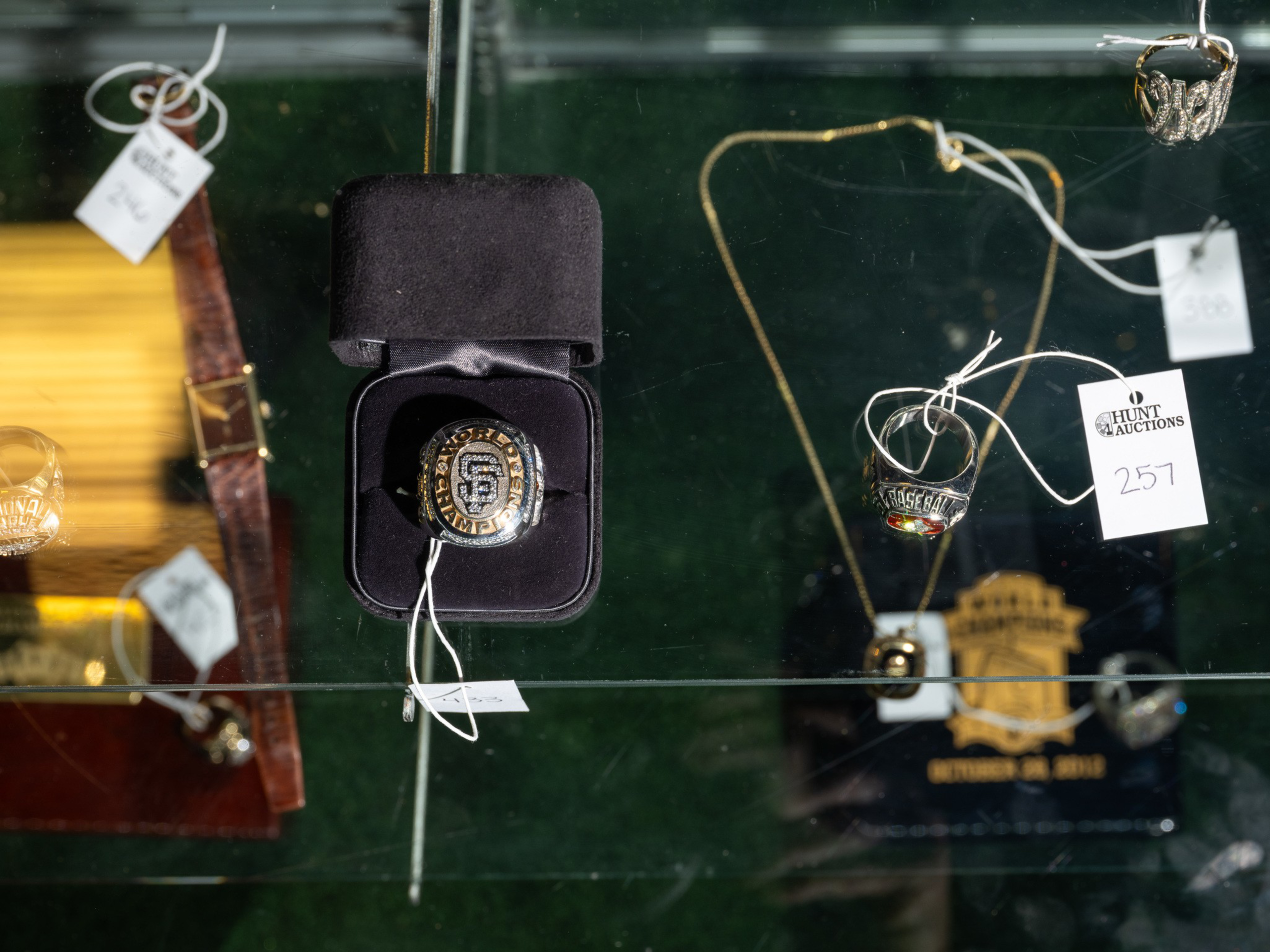 A collection of sports memorabilia including a San Francisco Giants championship ring in a black box, several rings, a watch, and a gold necklace with auction tags.