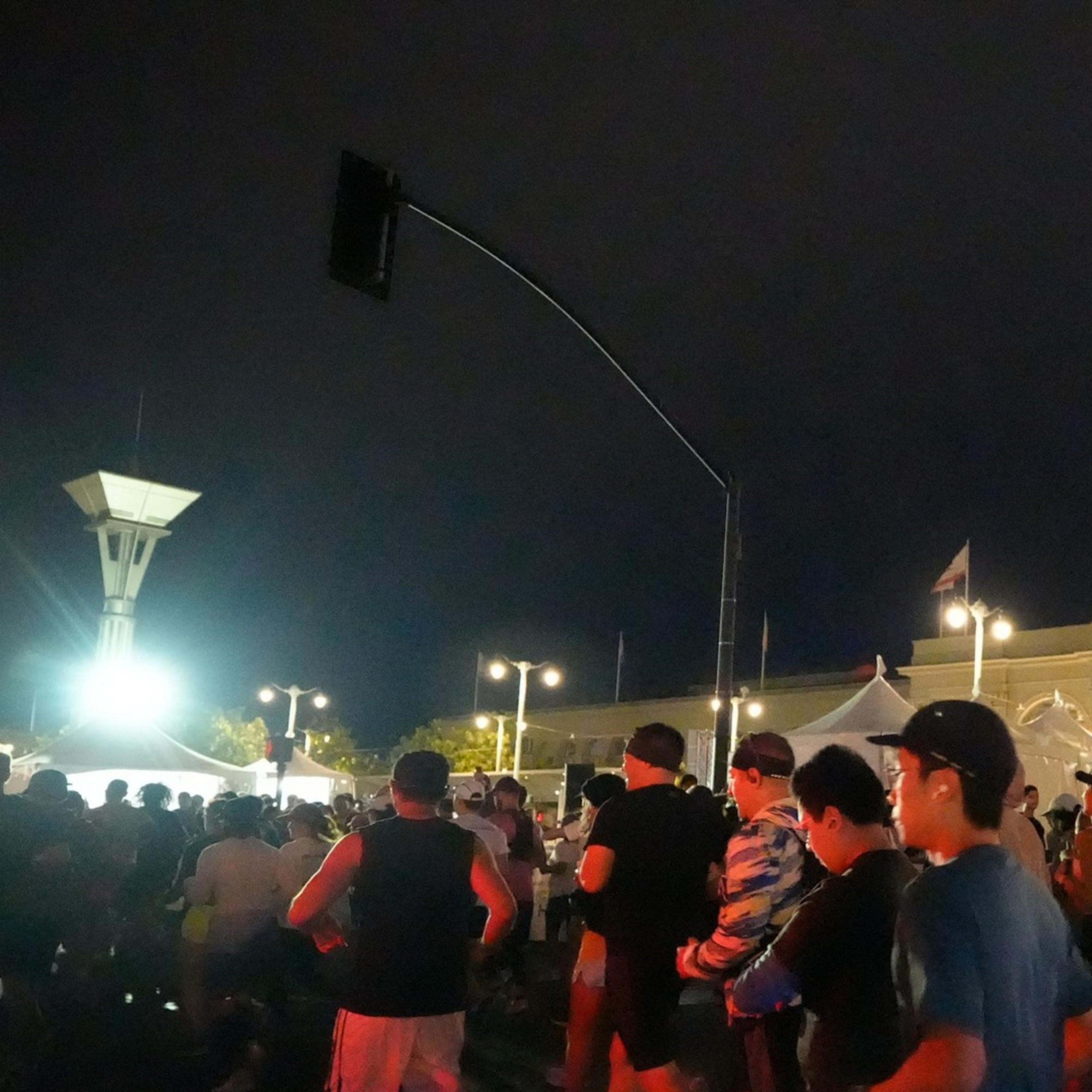 A group of runners is participating in a nighttime race, with an illuminated clock tower in the background. The scene is lively with people wearing athletic gear.