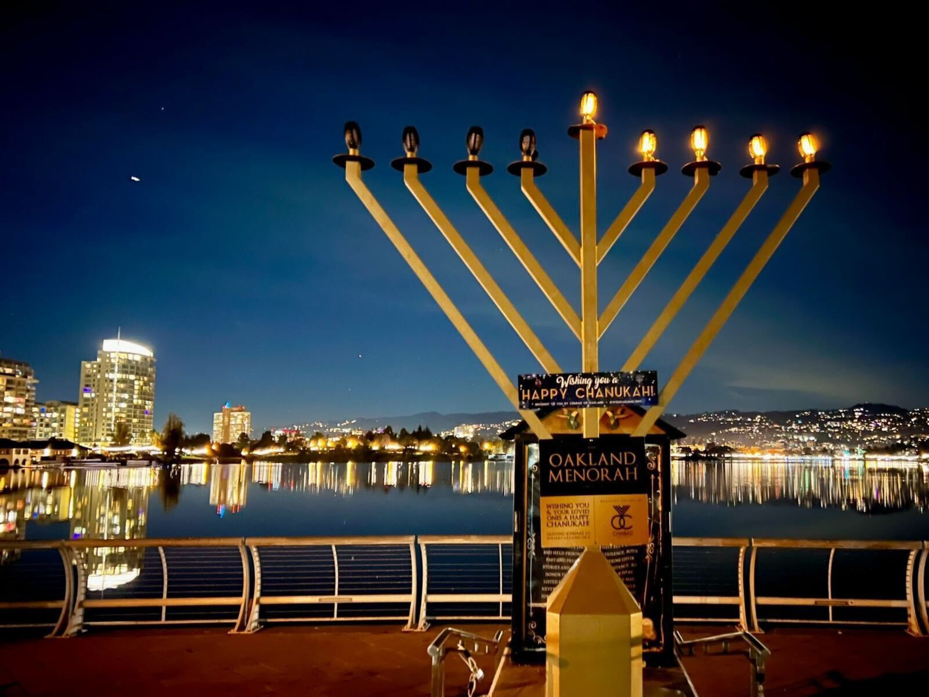 a menorah with a lake and a cityscape behind it.
