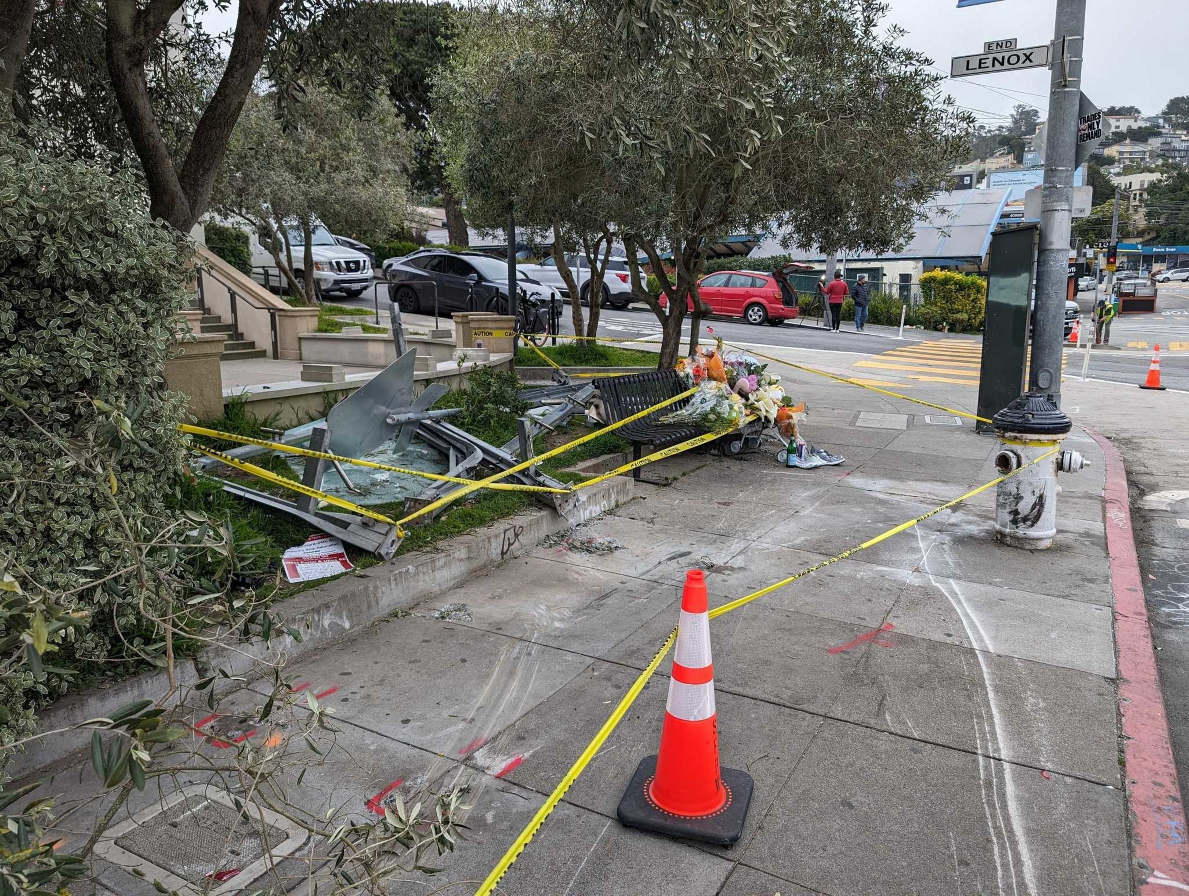 A damaged intersection with debris and caution tape, including a bent street sign, flowers on a bench, and traffic cones, suggests a recent accident.