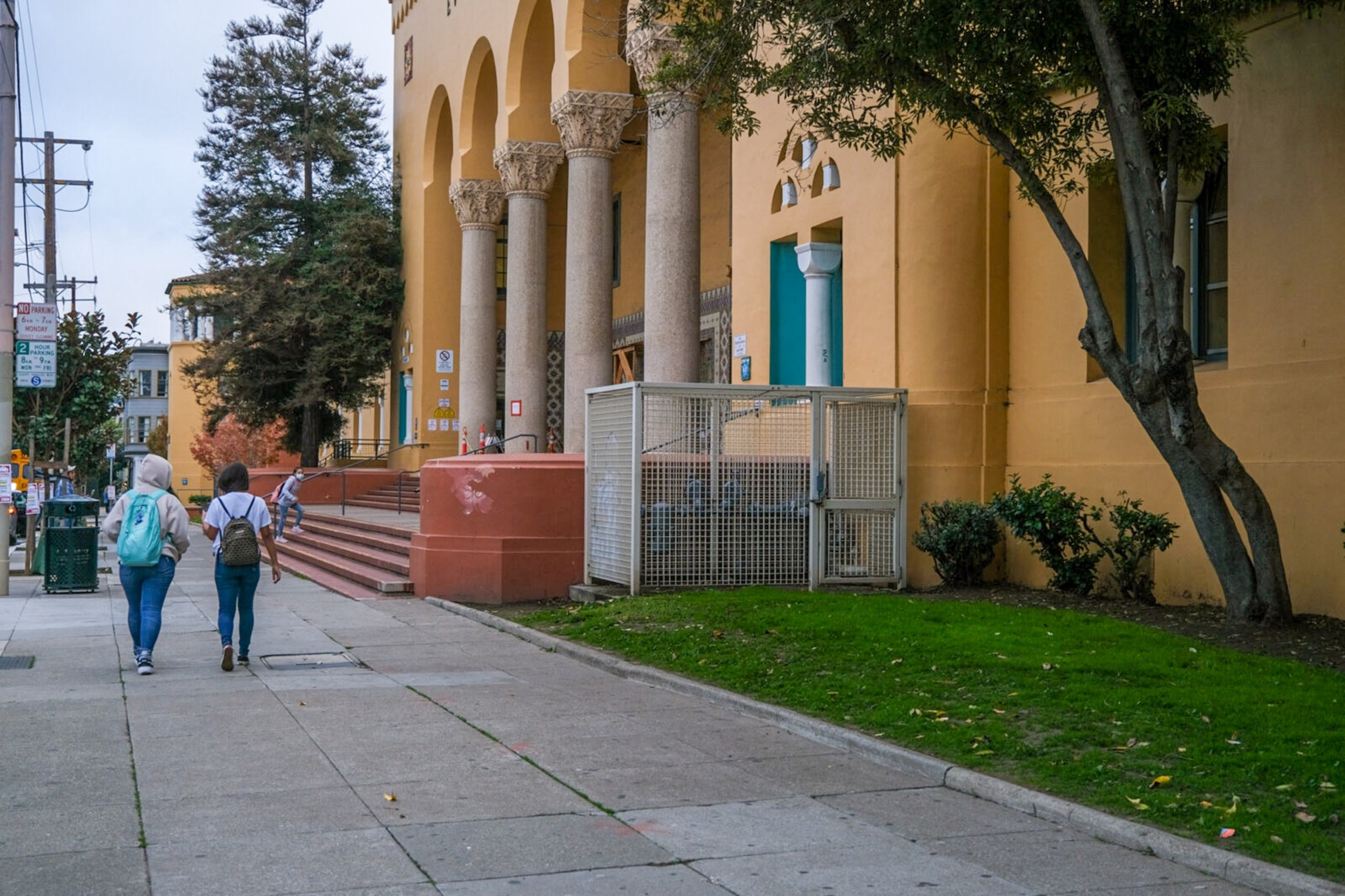 A school building is visible from a sidewalk outside.