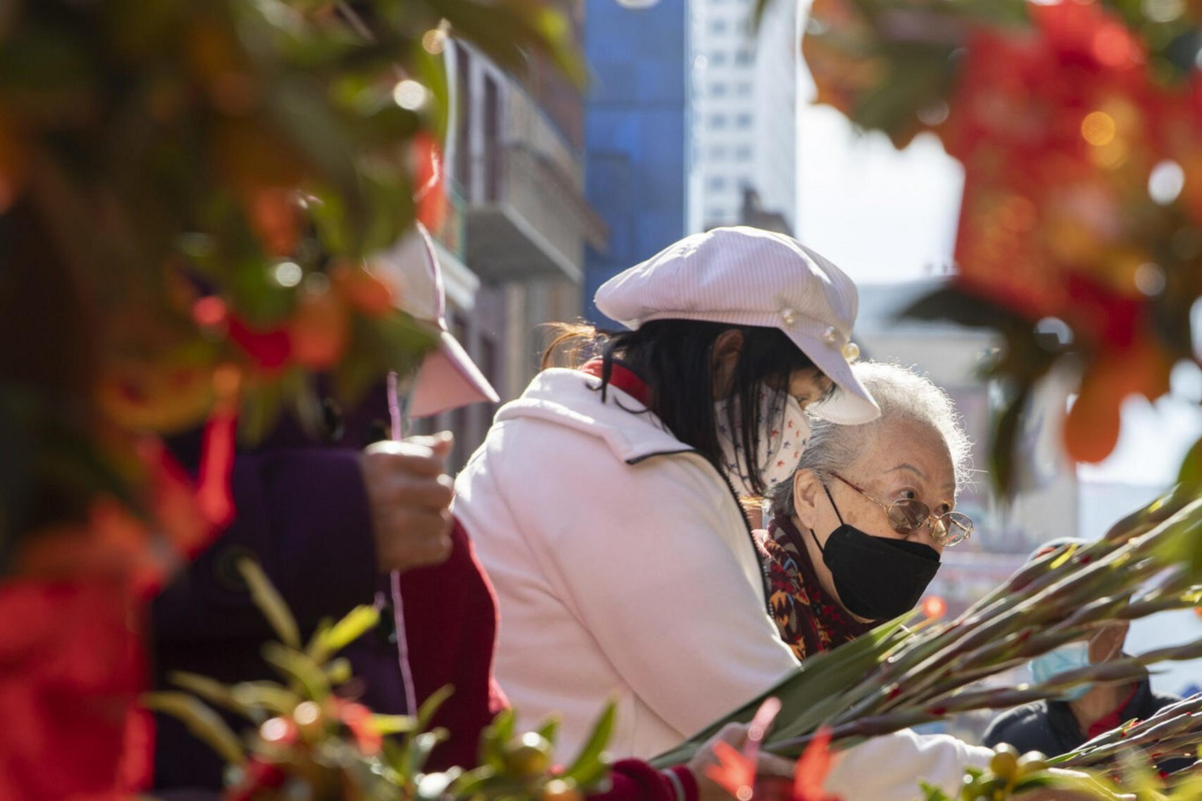 Two people, wearing masks, are browsing through a vibrant display of plants and decorations, with red and green colors prominently featured.