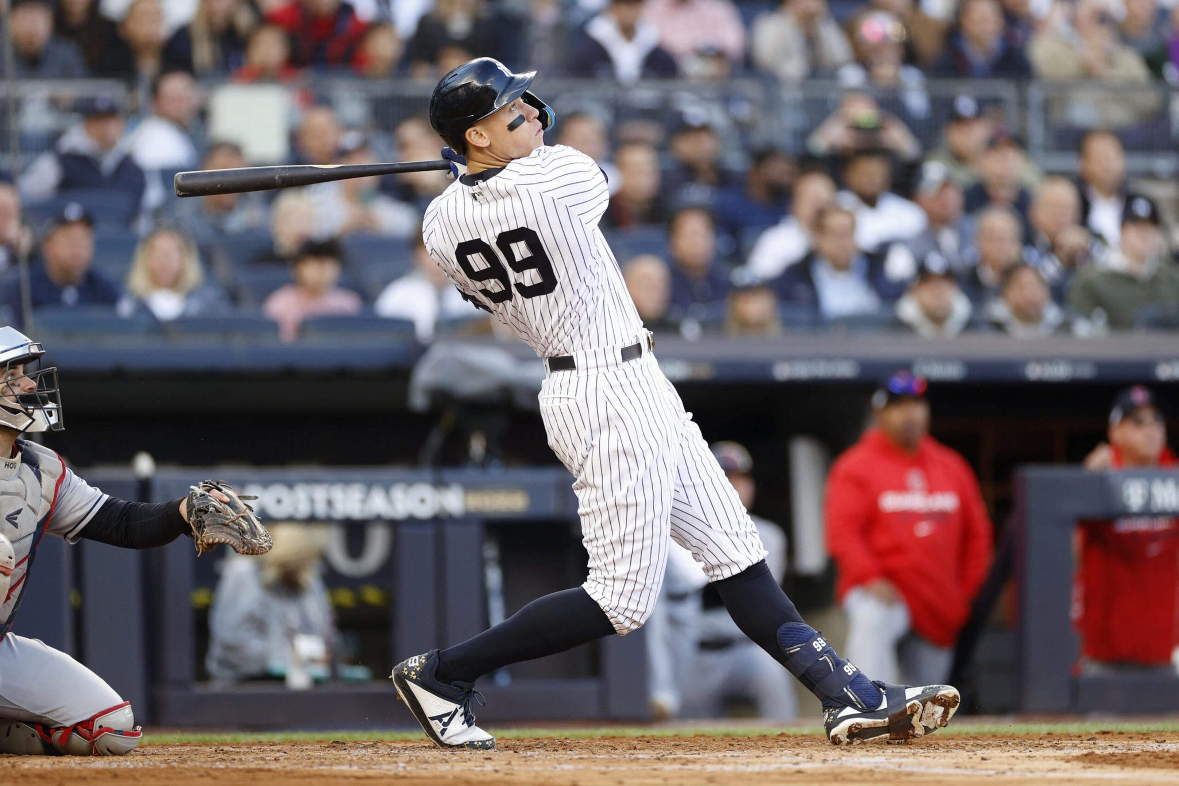 A baseball player in pinstriped uniform swings a bat while a catcher in gray and red gear prepares to catch the ball during a game.