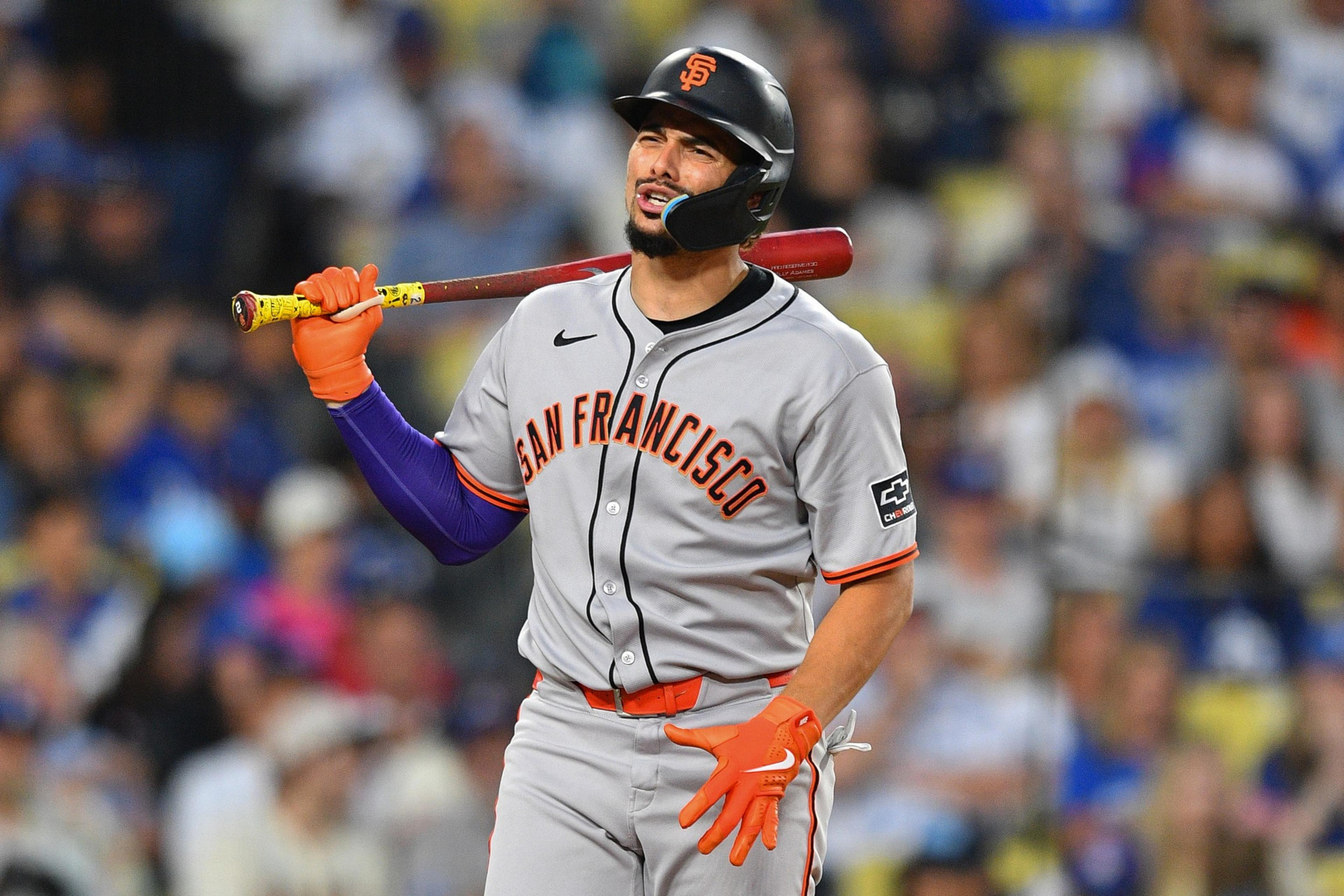 A baseball player in a gray "San Francisco" uniform holds a bat over his shoulder. He wears an orange glove and helmet, with a grimacing expression.