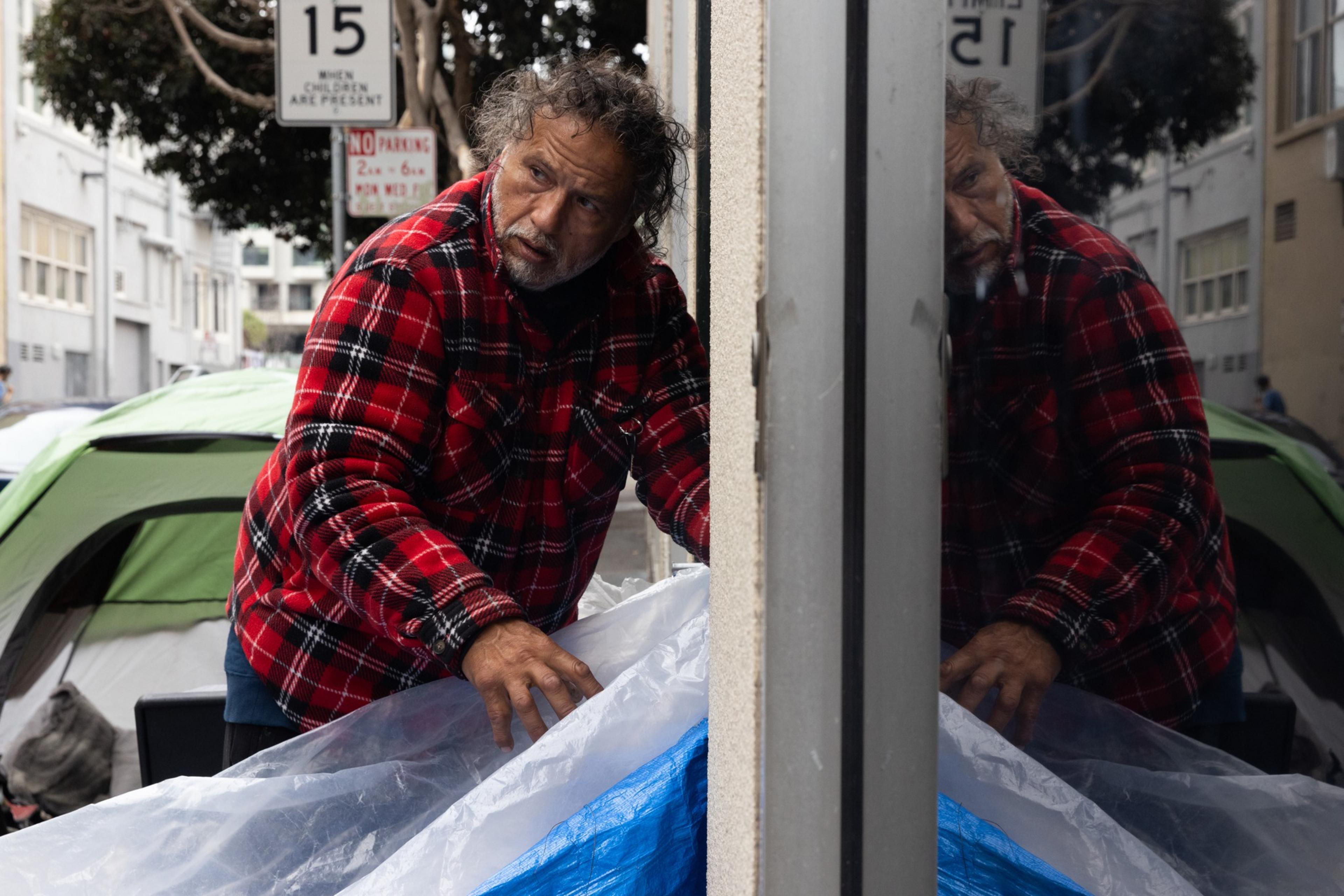 A man looks over his shoulder has he sets up his tarp along a building.