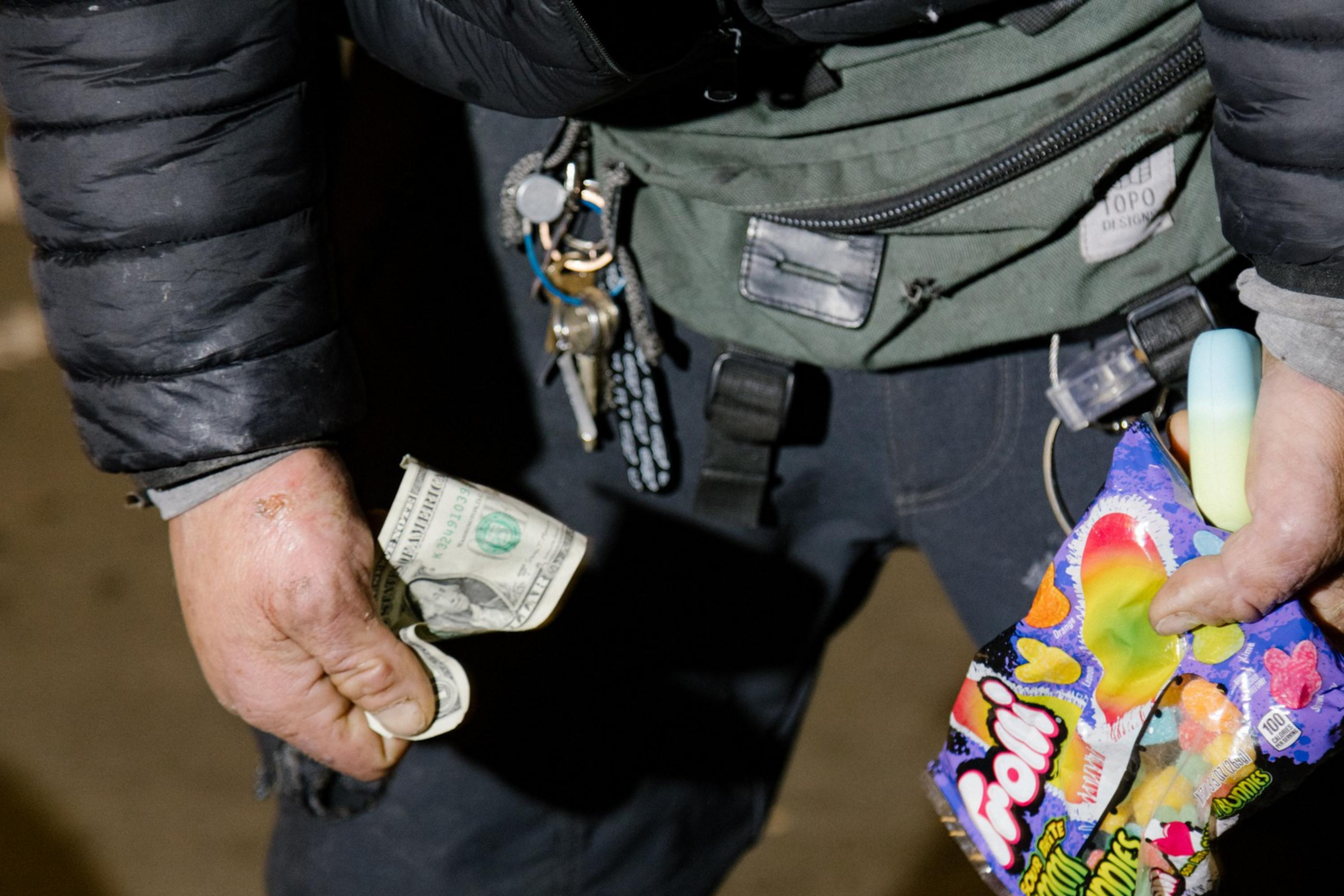 A man holds money, and candy for sale in his hands.