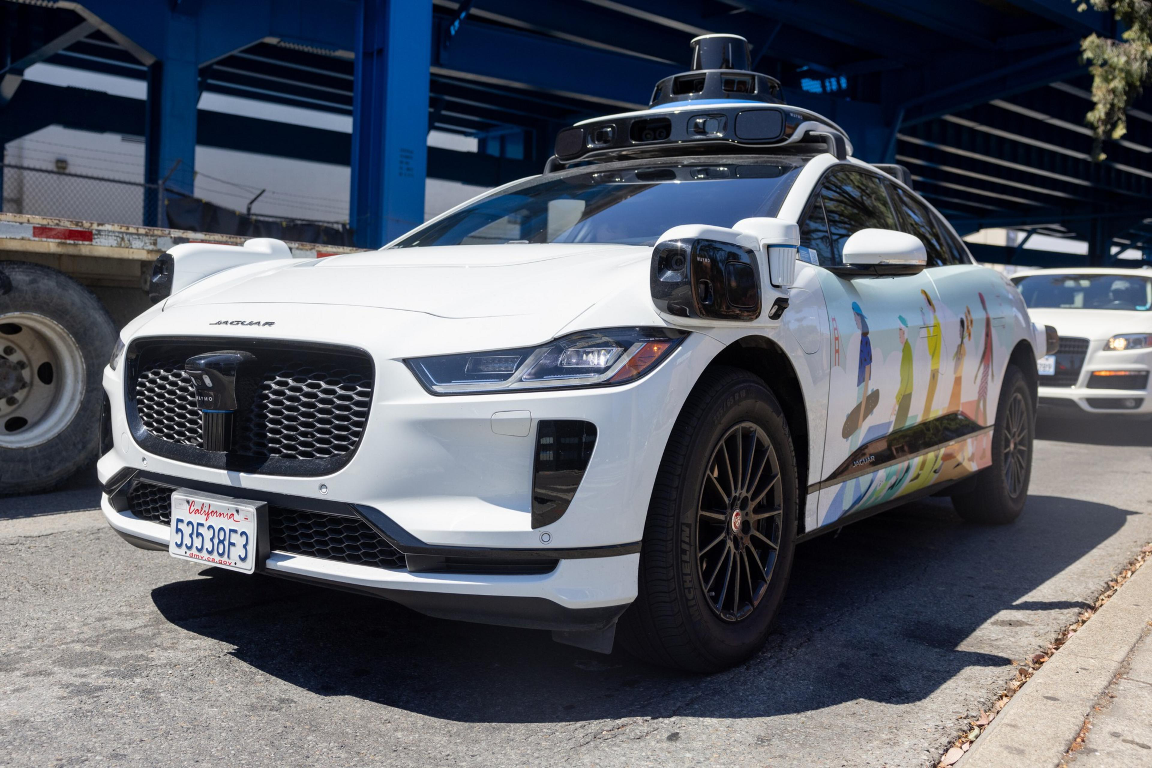 A white self-driving Jaguar I-PACE EV with sensors and cameras mounted atop and on its sides.