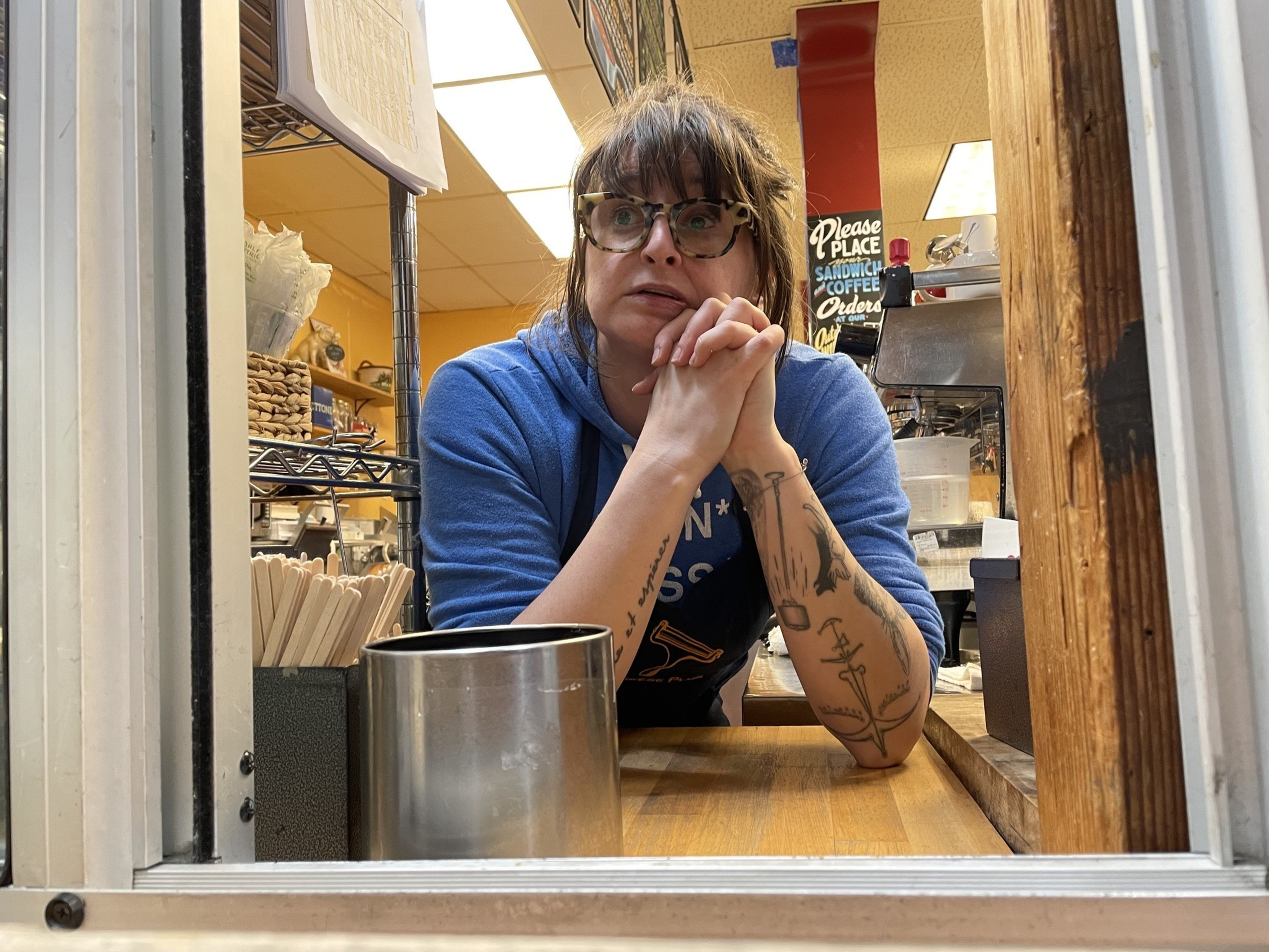 A woman stares through a window, resting her cheek on her hands.