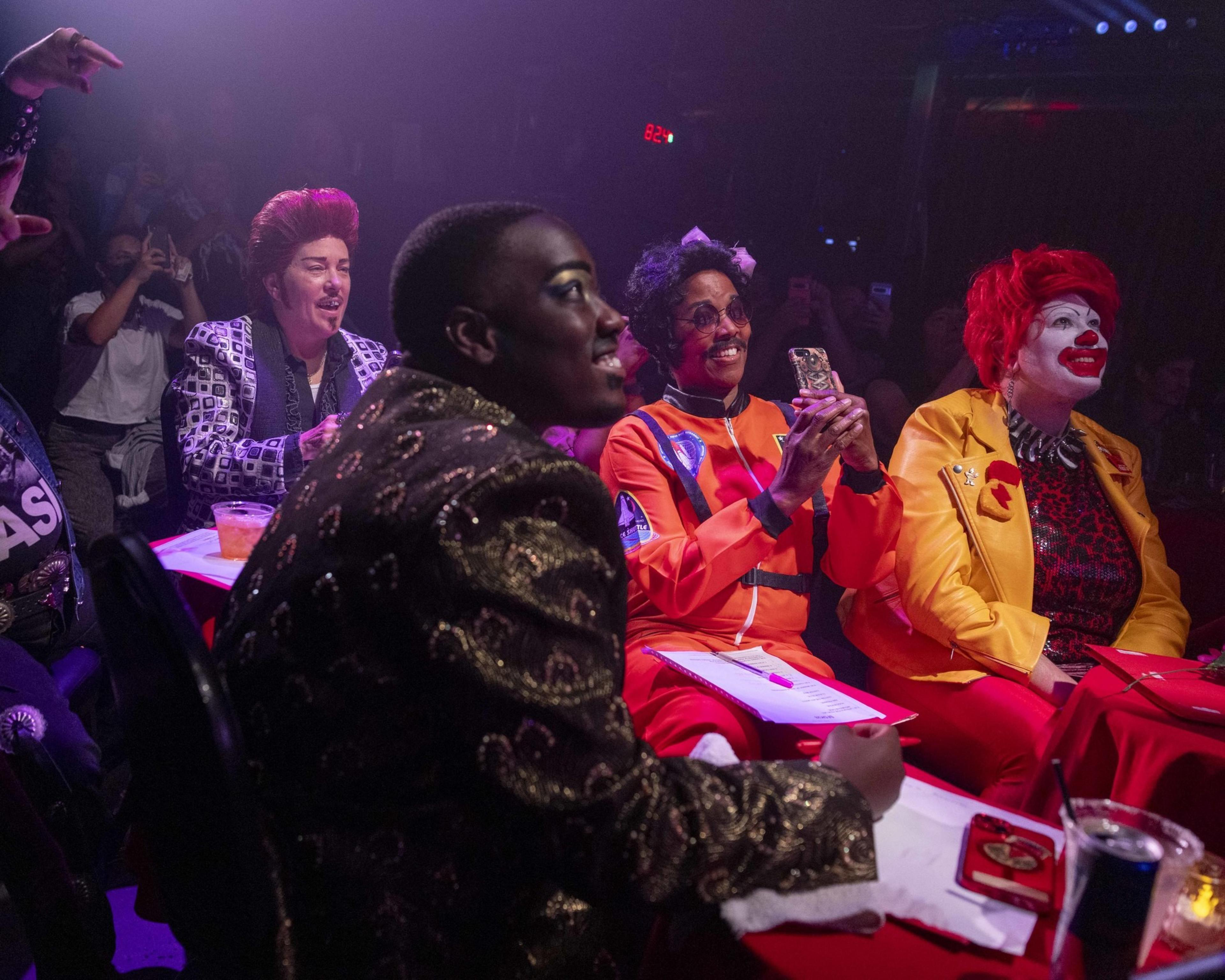 Judges in fancy dress watch a show, one looks like Ronald McDonald.