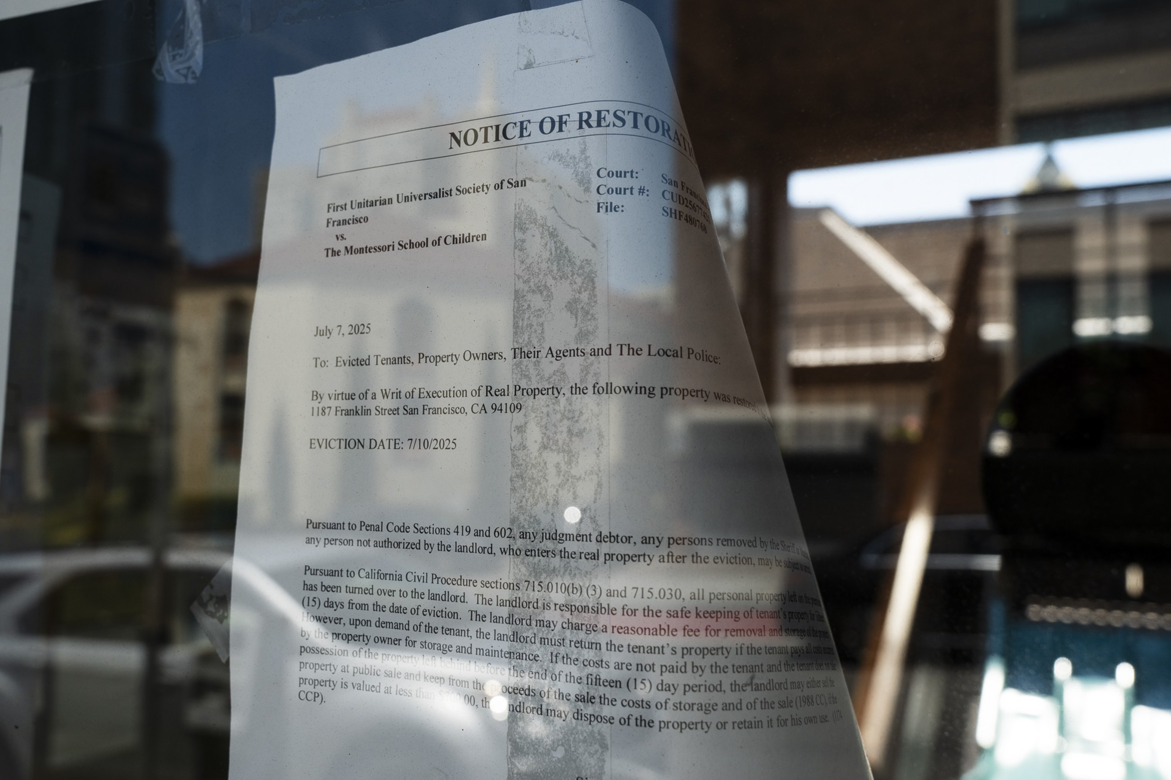A legal notice about property restoration is taped to a window. It contains information about eviction, addressed to tenants and owners, with a building reflected behind.