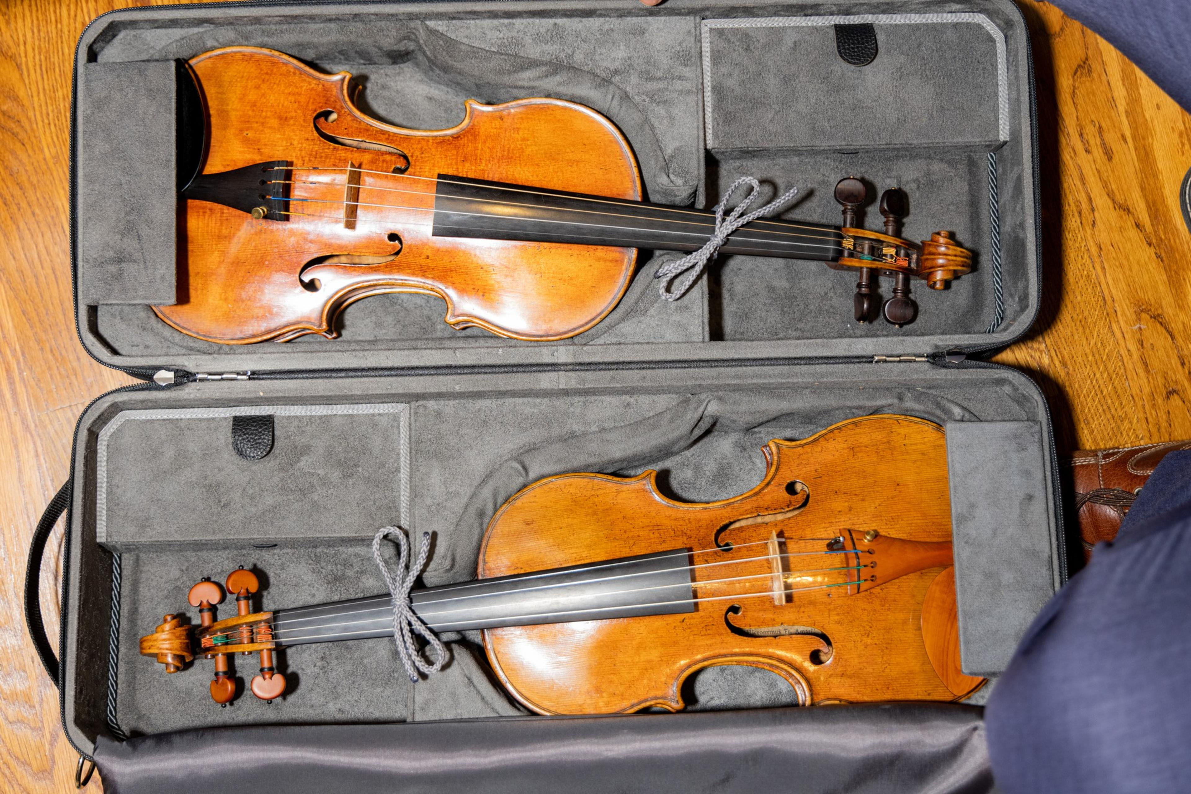 Two violins sit in their case, glowing in the light
