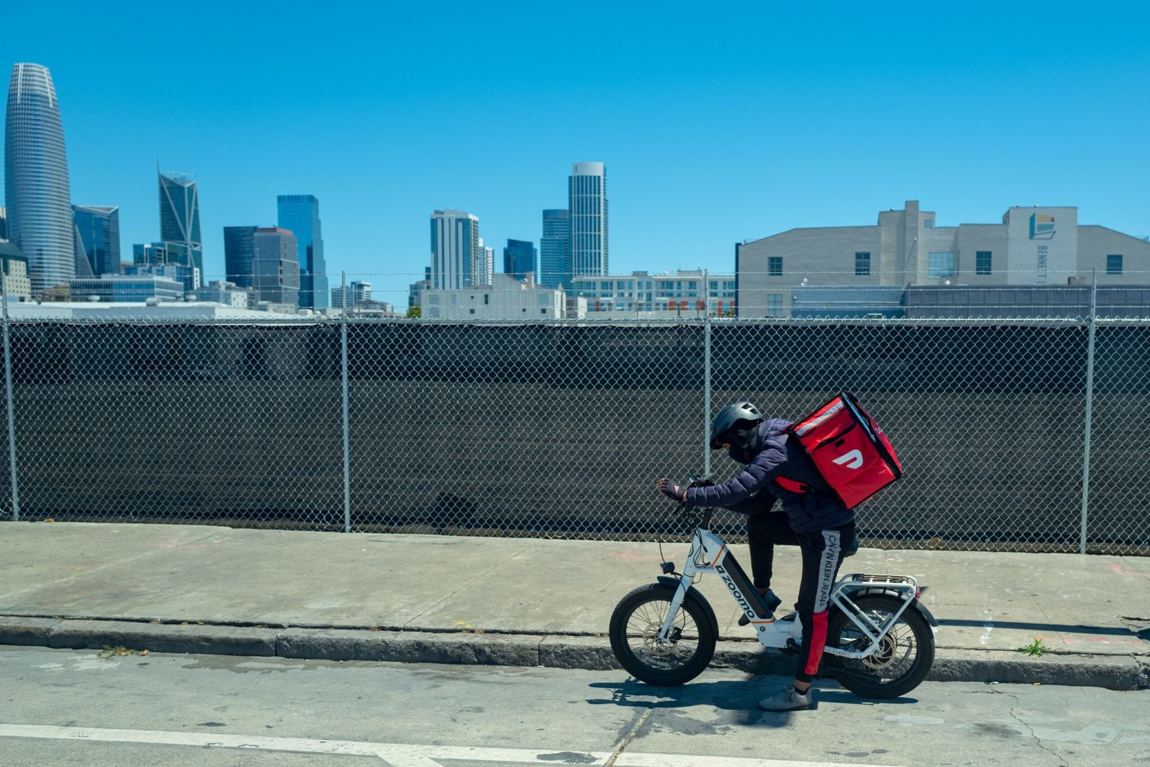 A person rides a bike with a cooler on their back.