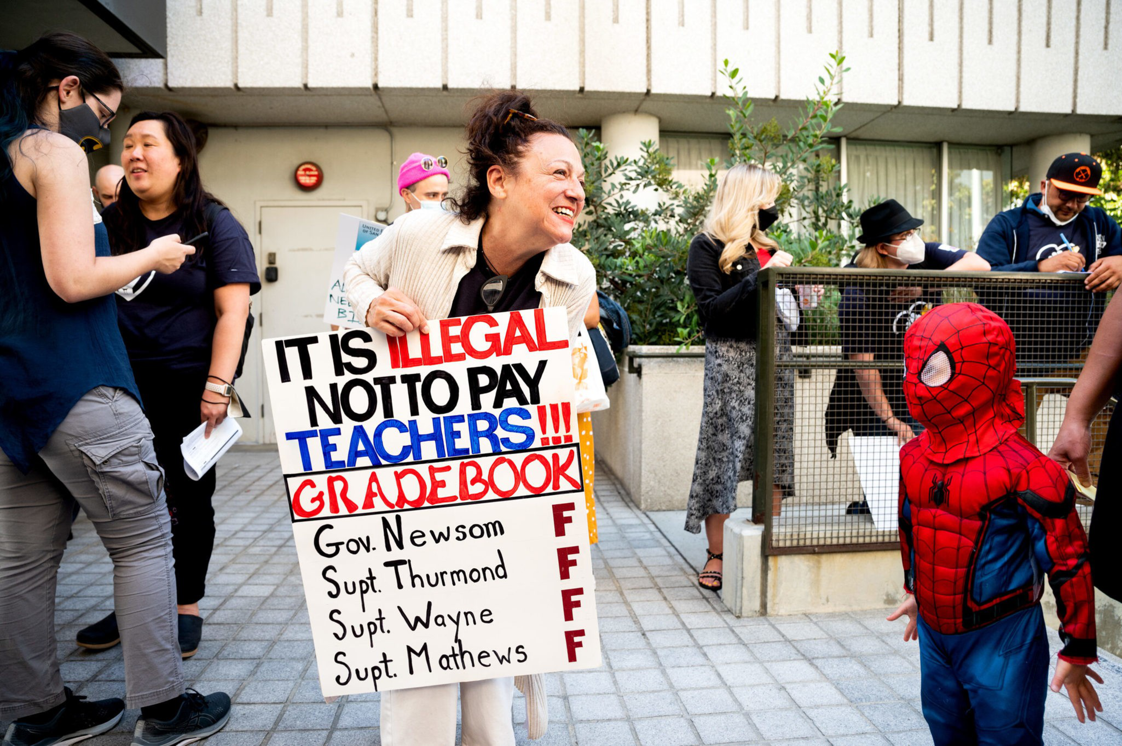 Former Lincoln High School Spanish teacher Mary Cerasoli holds a sign before attending a SFUSD Board of Education meeting on Tuesday, Aug. 9, 2022, in San Francisco. At right is Felix Lang, 3, whose mom is a teacher. | Noah Berger for The Standard
