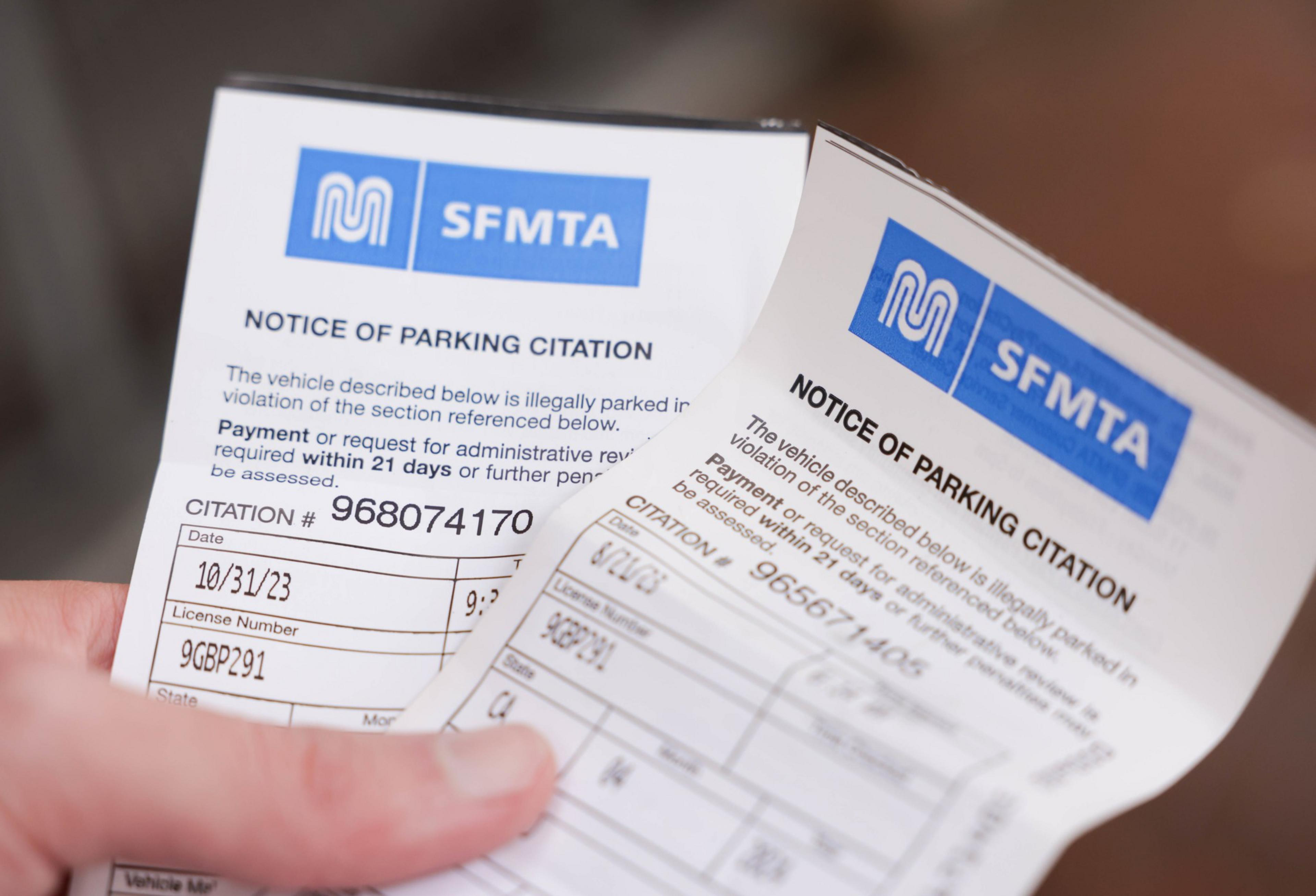 A man holds two parking tickets.