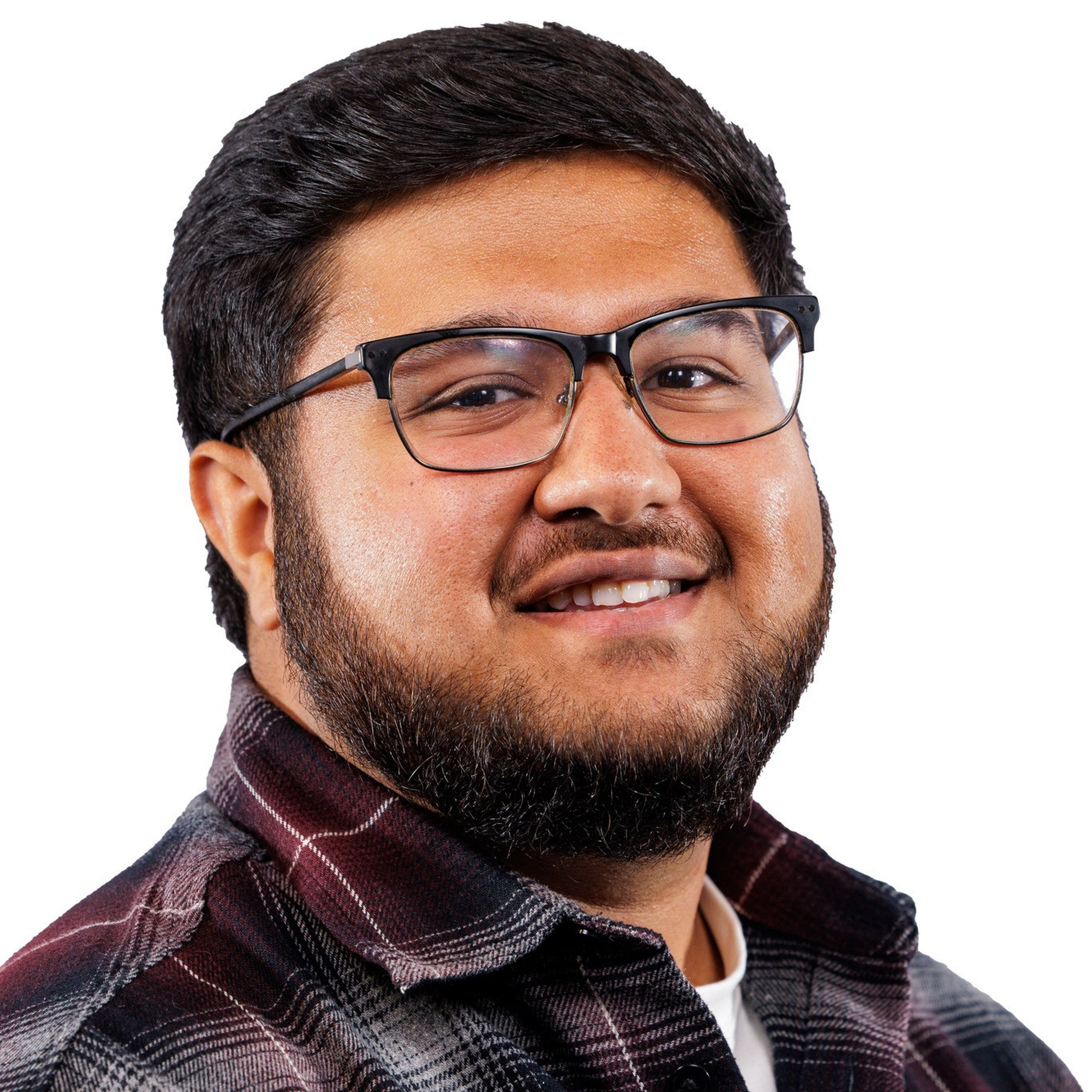 A smiling man with short black hair, glasses, and a beard wears a dark red and black plaid shirt over a white t-shirt against a white background.