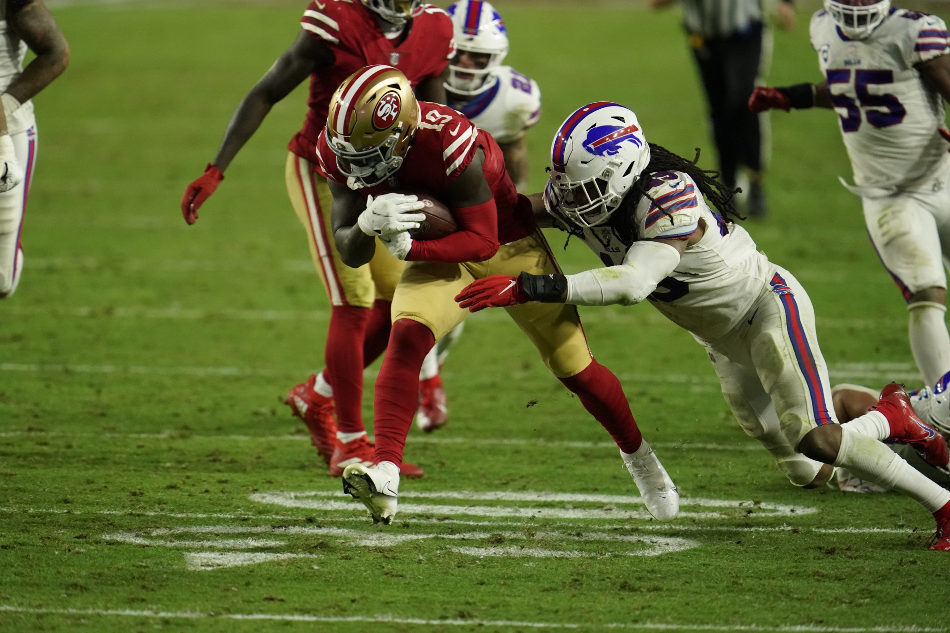 A player in a red uniform is running with the football, tightly pursued by a player in a white uniform attempting a tackle on a grassy field.