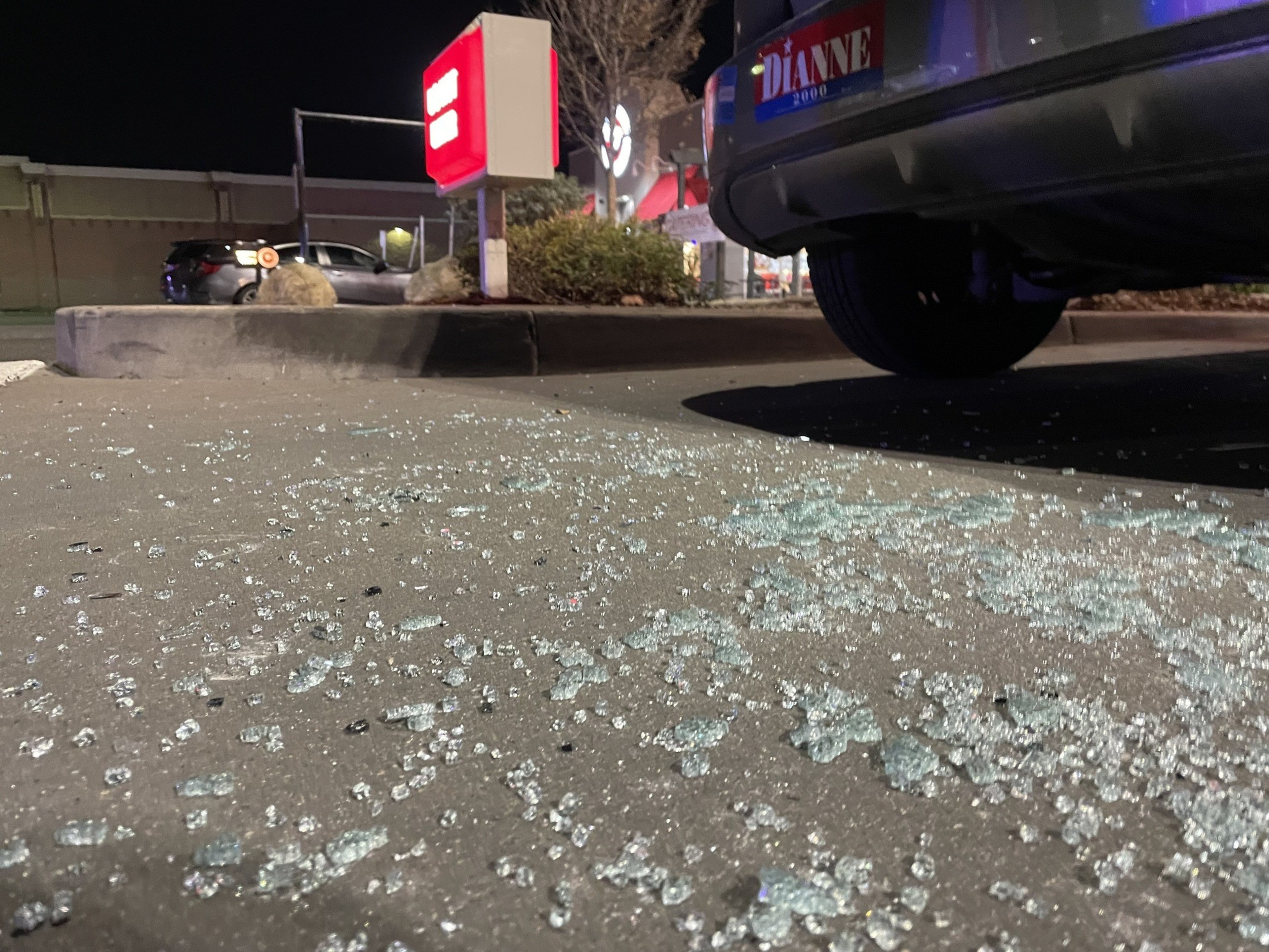 Smashed glass litters the pavement near a parked car.