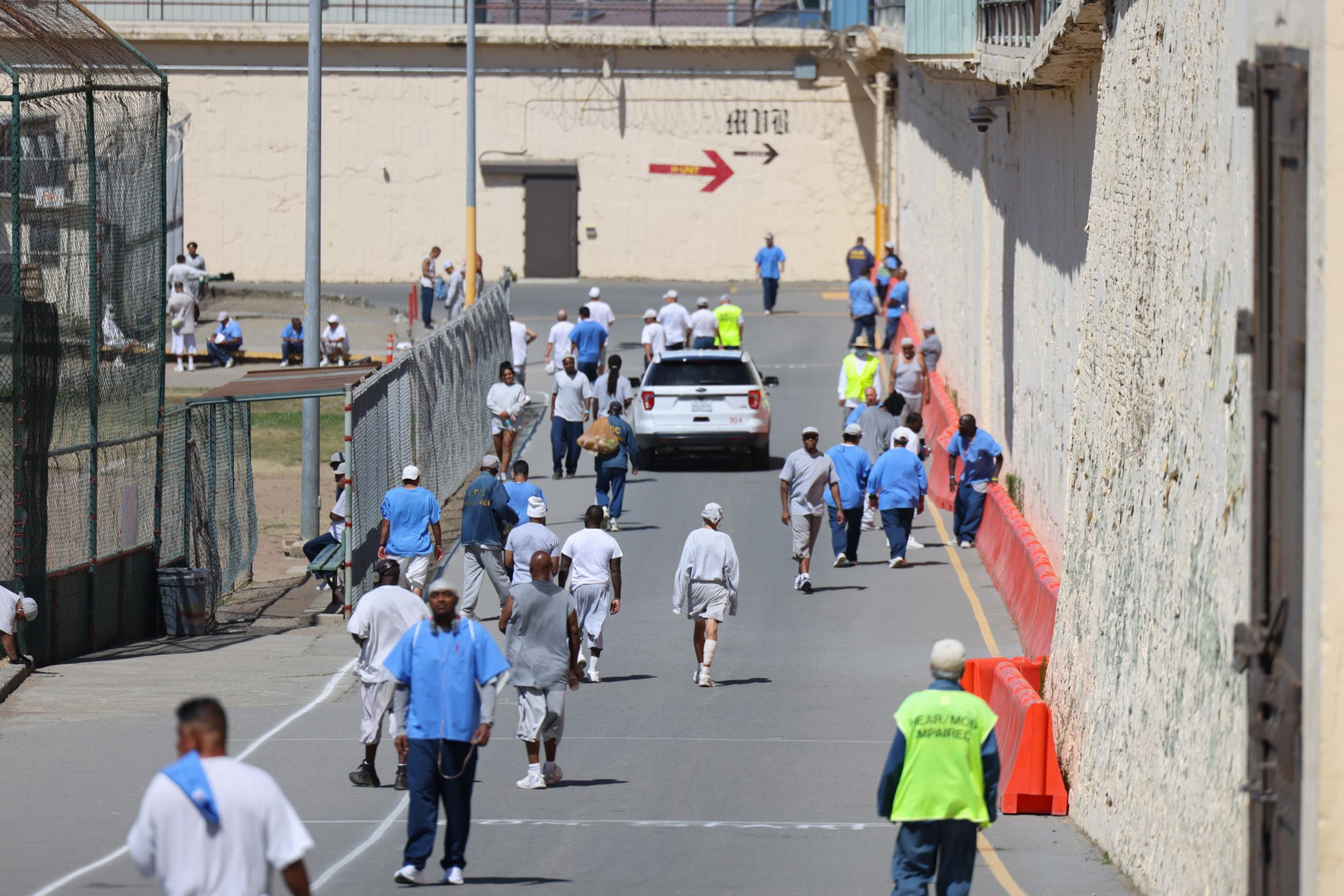 People walk down a paved roadway next to a chain link fence