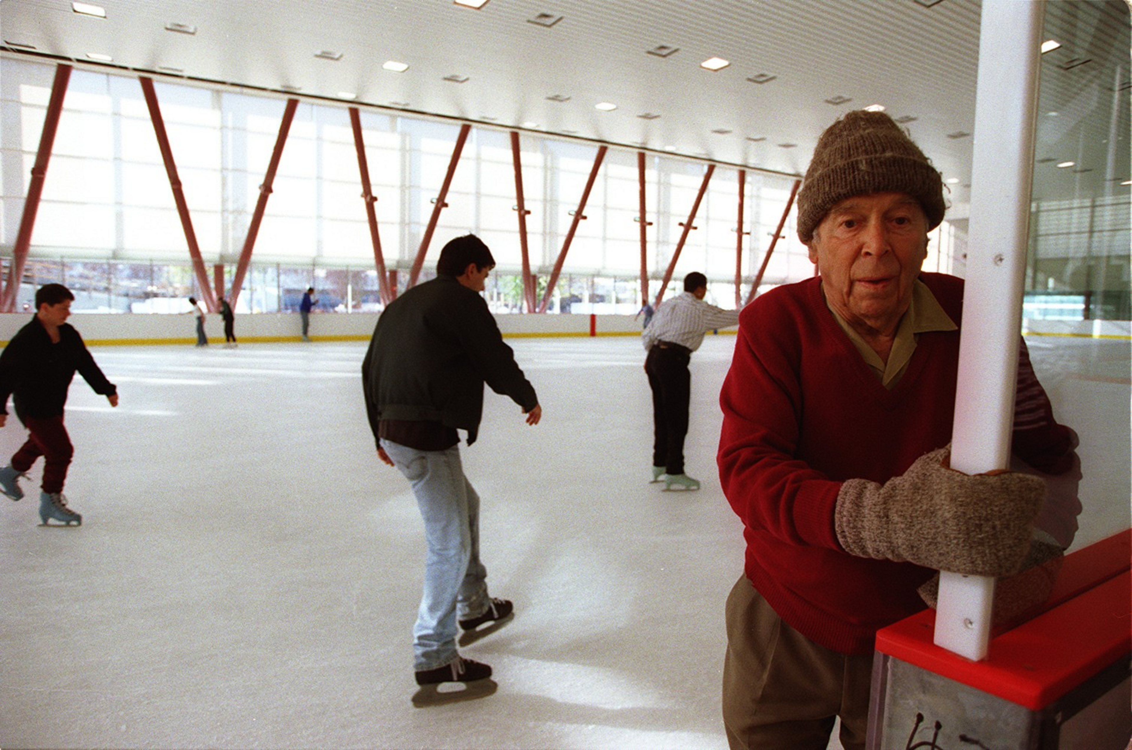 An elderly man in a red sweater and knit hat holds a pole at an indoor ...