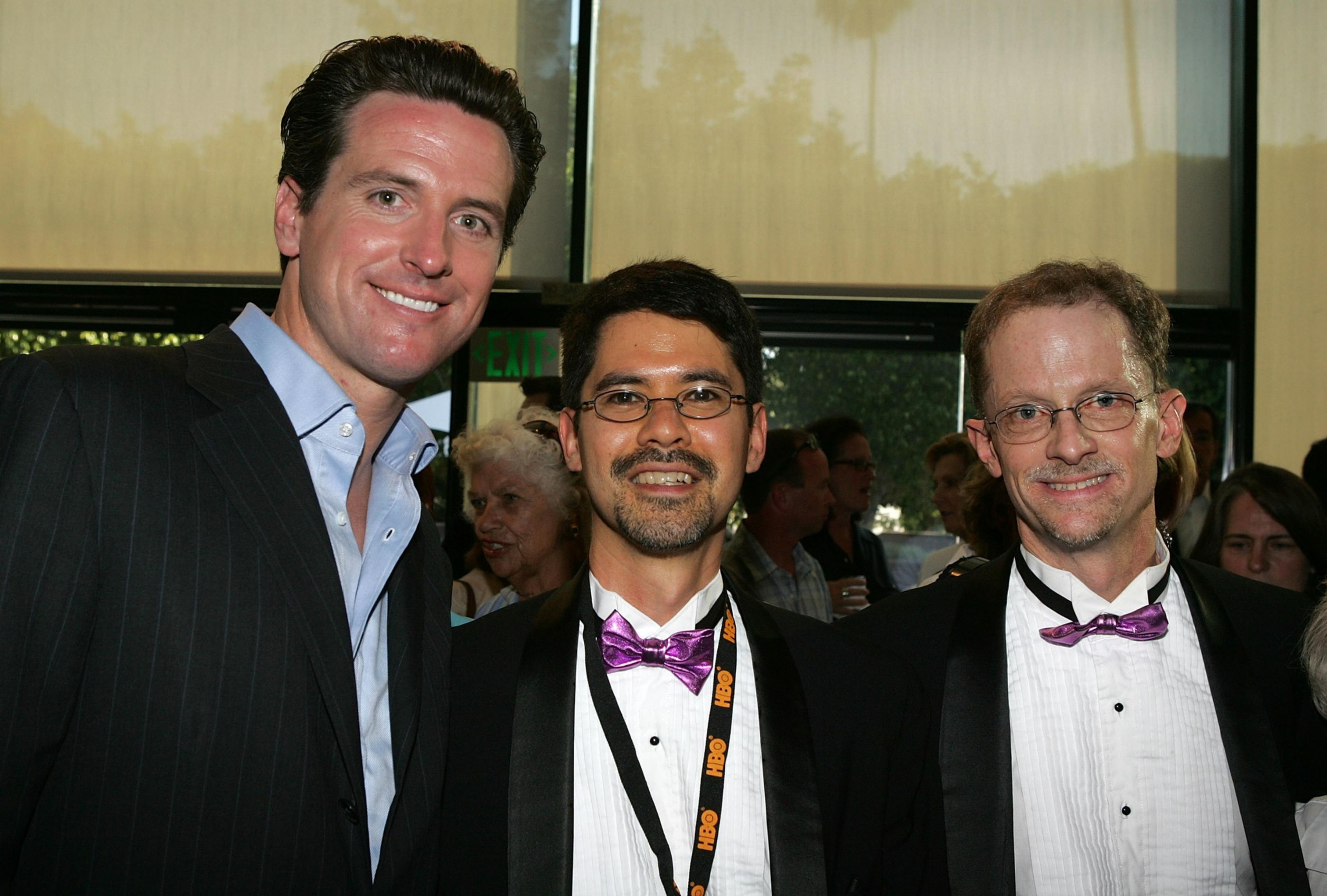 Three men wearing suits stand together smiling for a photo.