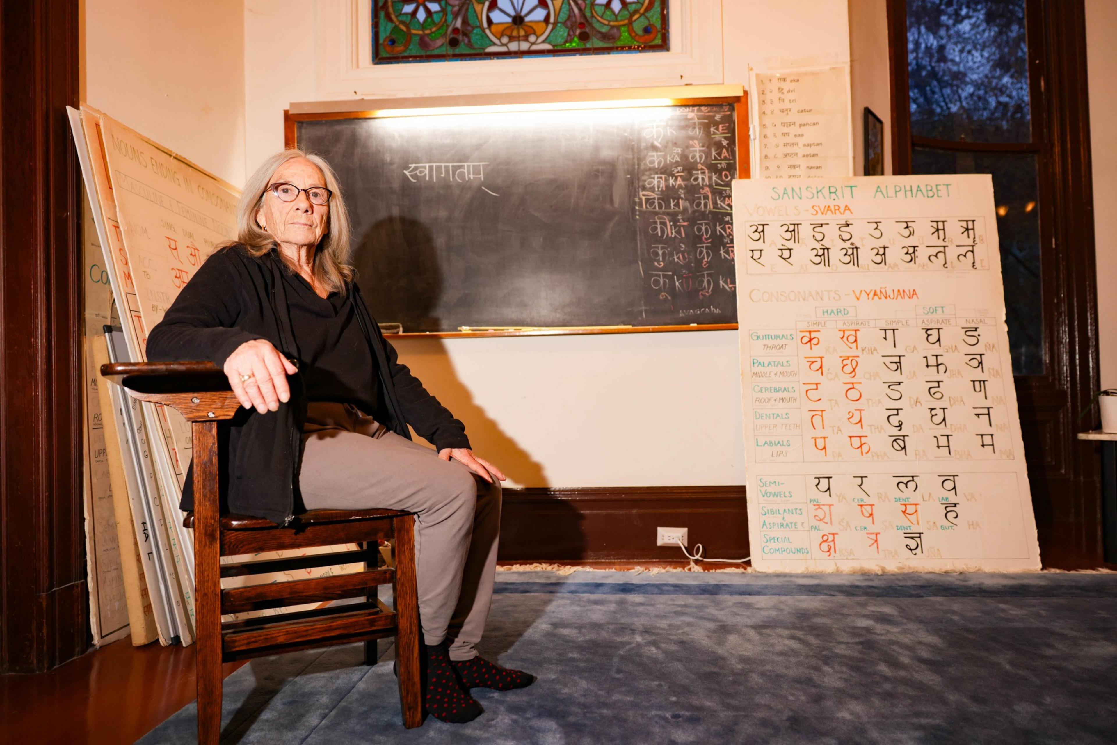 A person seats in a school chair with a black board and poster boards in the background.