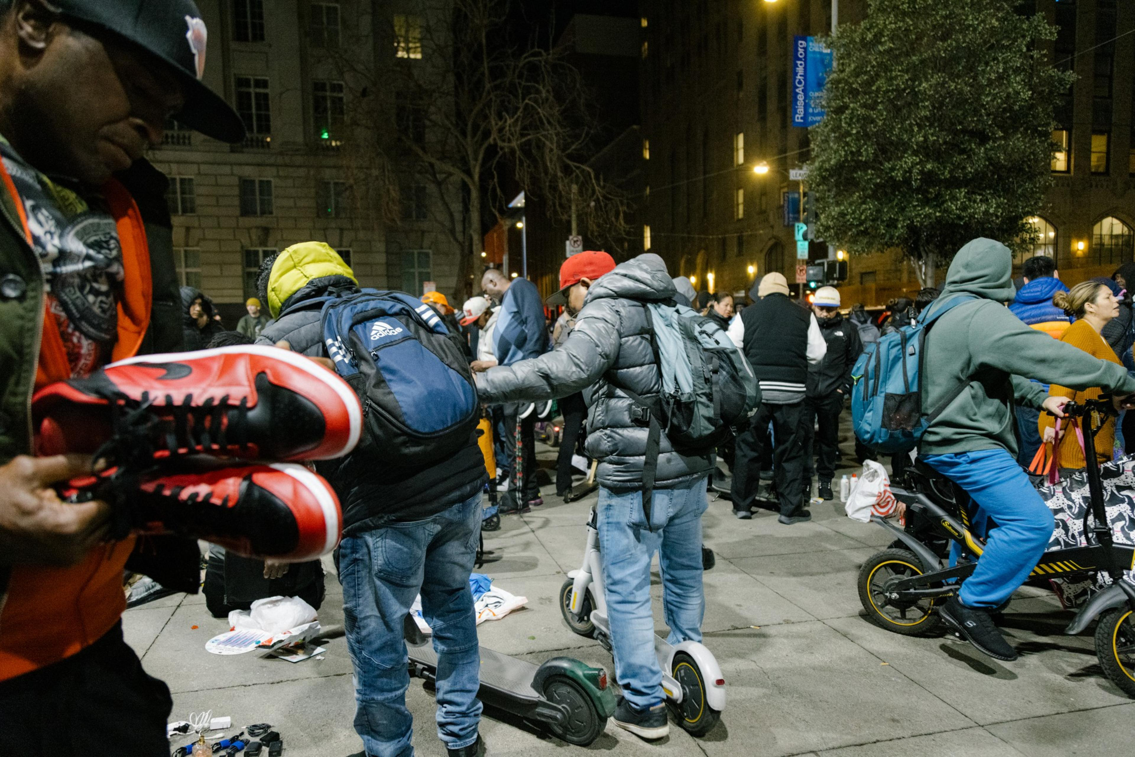 A bustling street scene at night with people on scooters and a close-up of someone holding red sneakers.