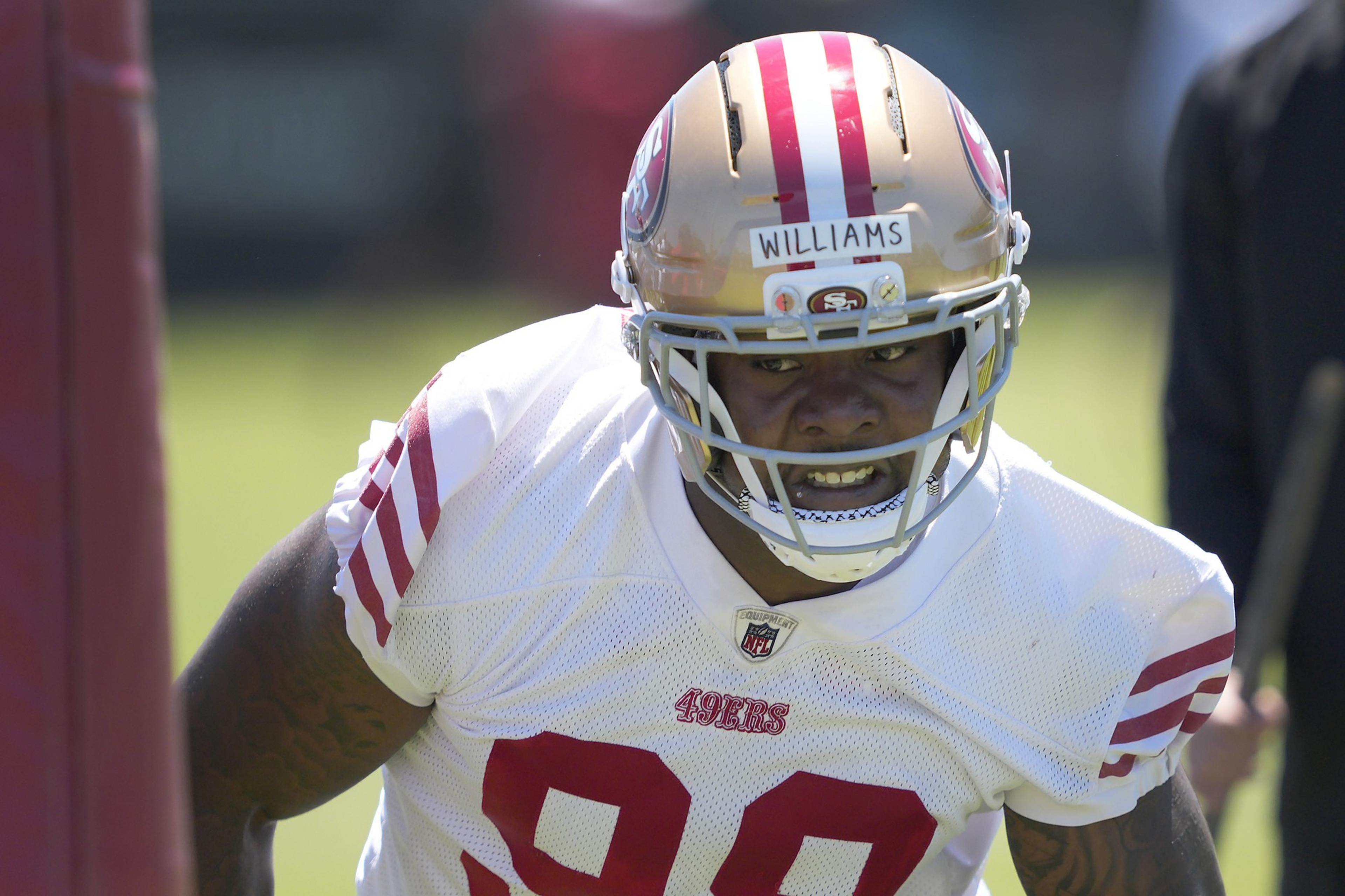 An athlete wearing a football helmet and white jersey with red stripes, marked &quot;49ers&quot; and number 90, is intensely focusing during training.