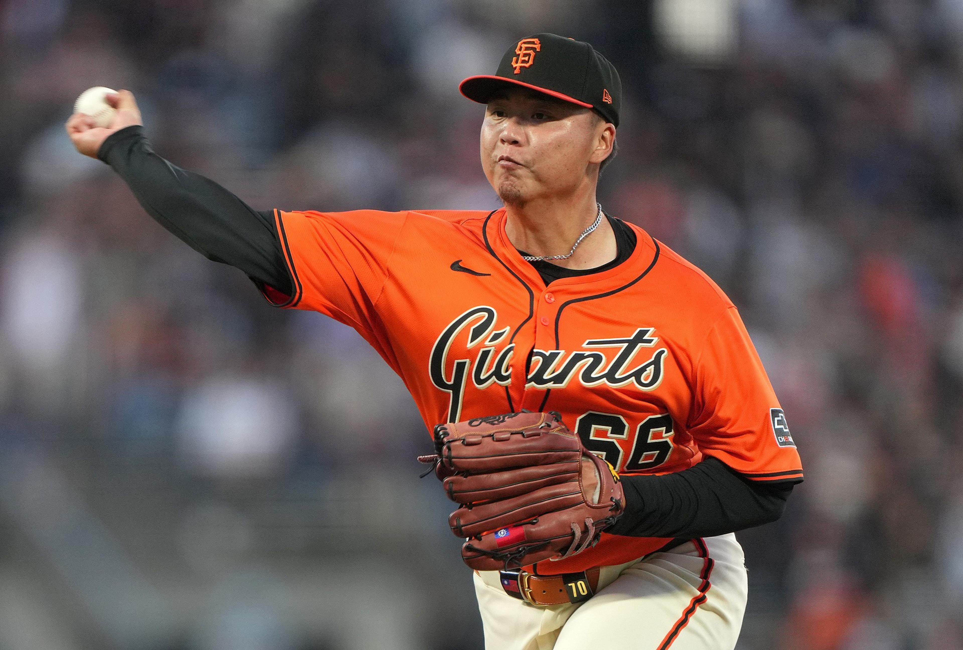 A baseball player wearing an orange Giants jersey and black cap is pitching a ball with focus and intensity.