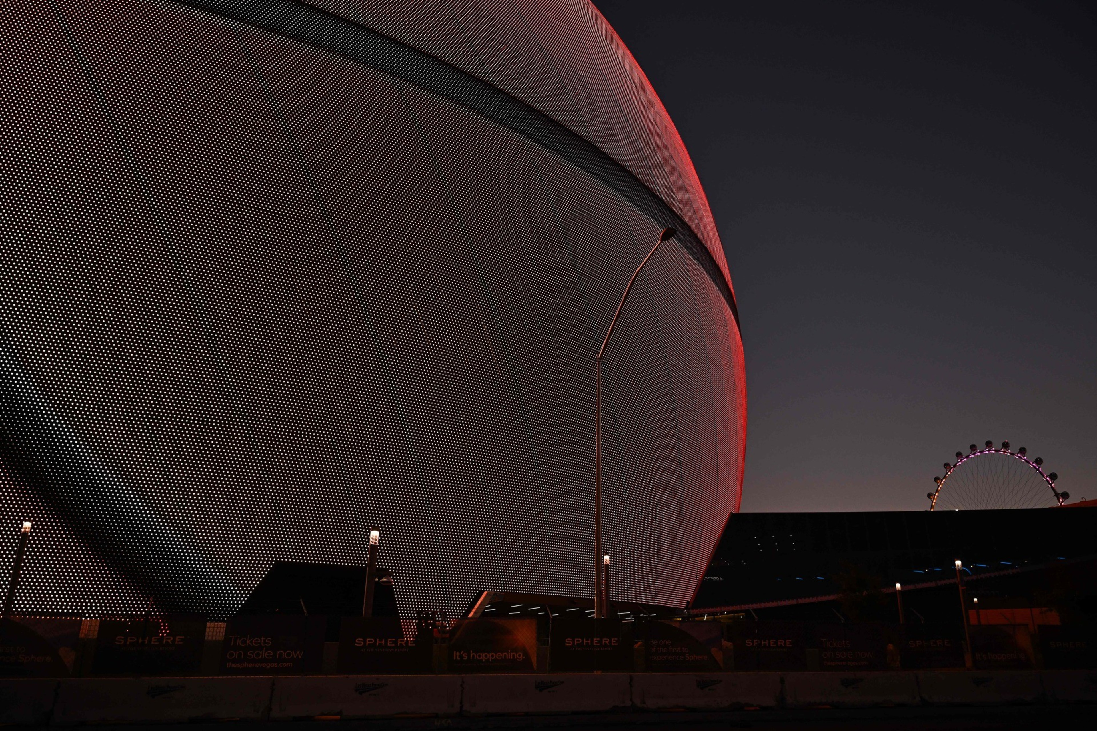 A large, textured sphere is lit in red against a dark sky. In the background, a faint Ferris wheel is visible, and a few streetlights are illuminated.