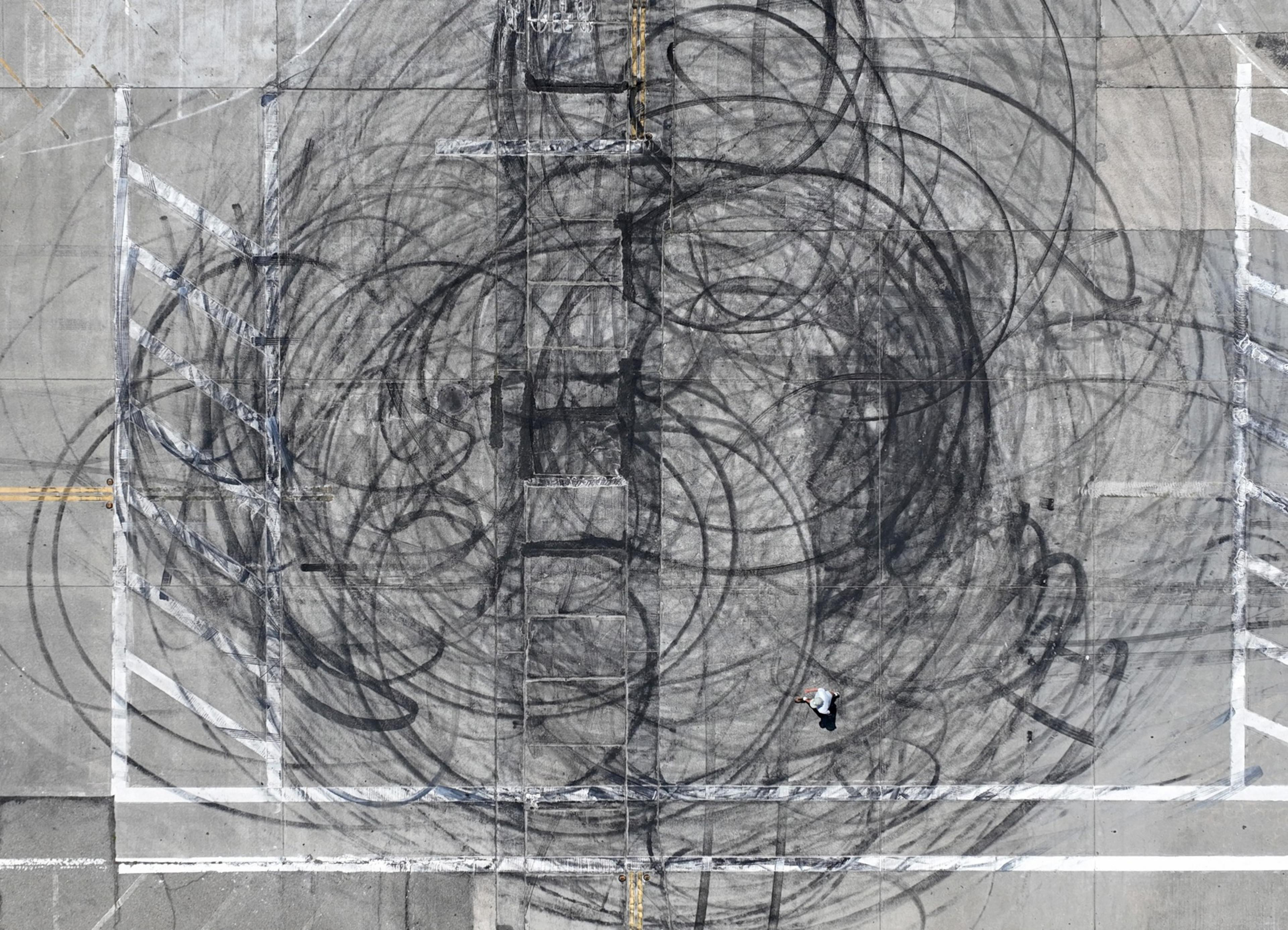 Circular black marks left on roadway tarmac litter an intersection seen from above in daylight after nighttime stunt driving